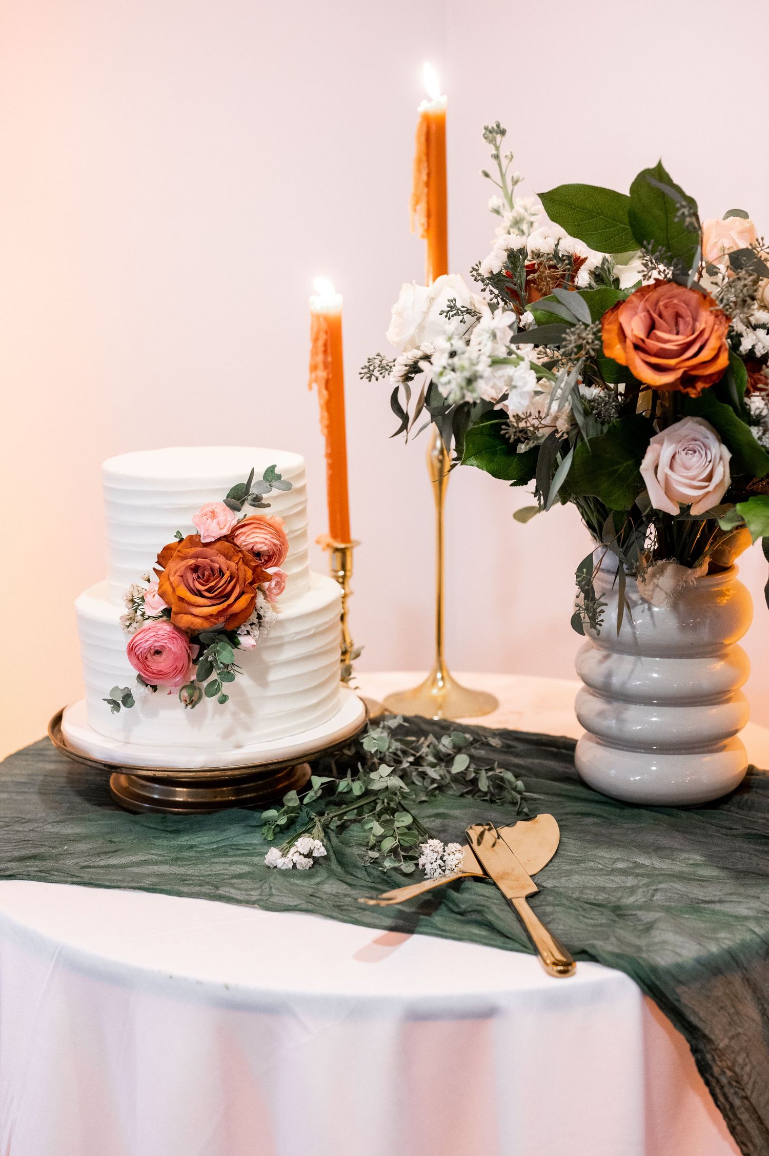 Wedding cake display with orange taper candles and romantic floral arrangements.