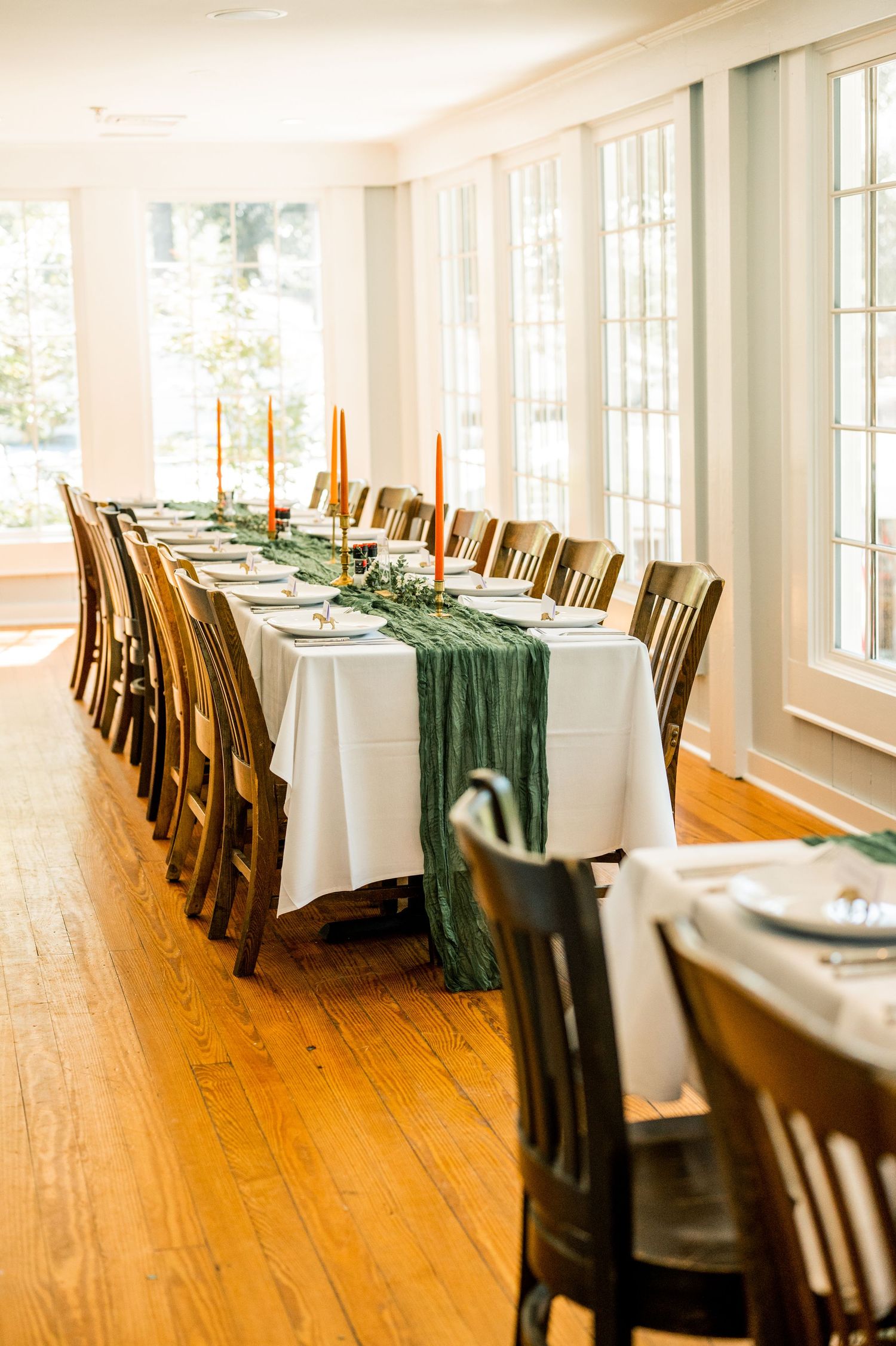 Long banquet room with white tablecloths and wooden chairs set for an elegant reception.