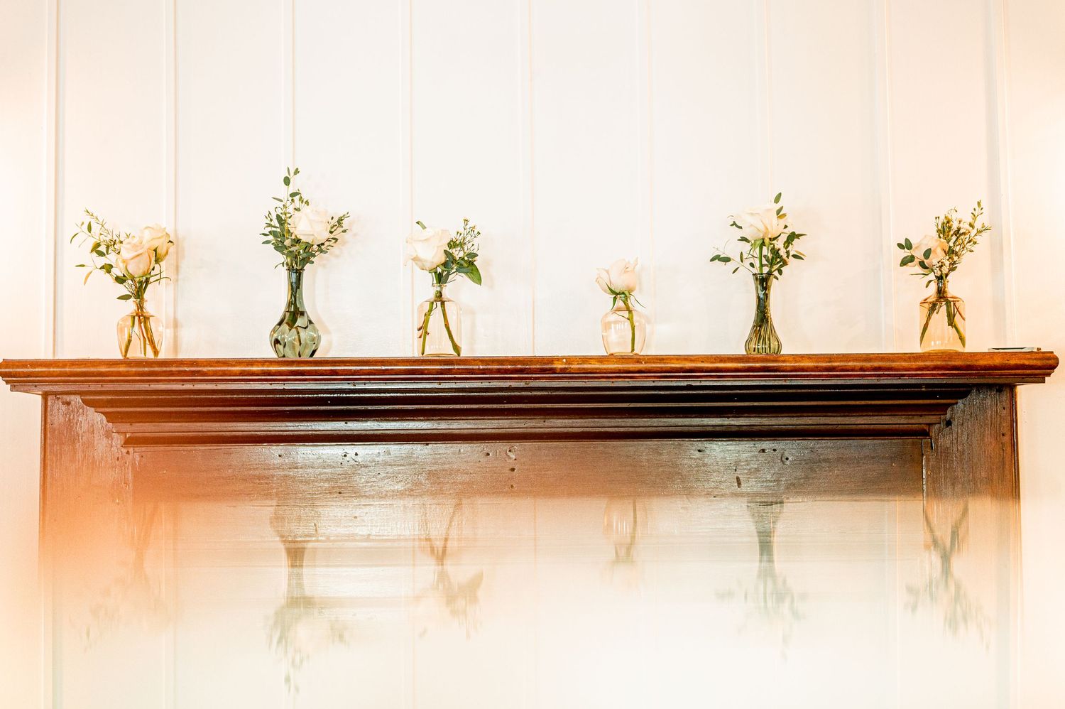 Row of small glass vases with delicate floral arrangements displayed on wooden shelf.