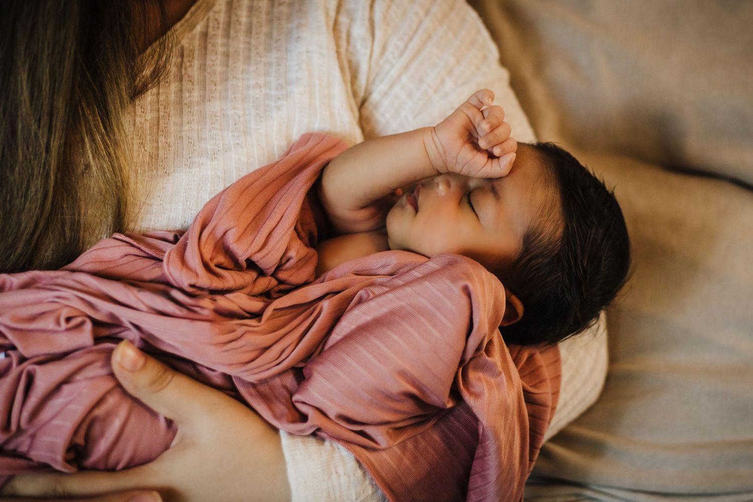 Child in pink clothing sleeping peacefully on light colored couch.