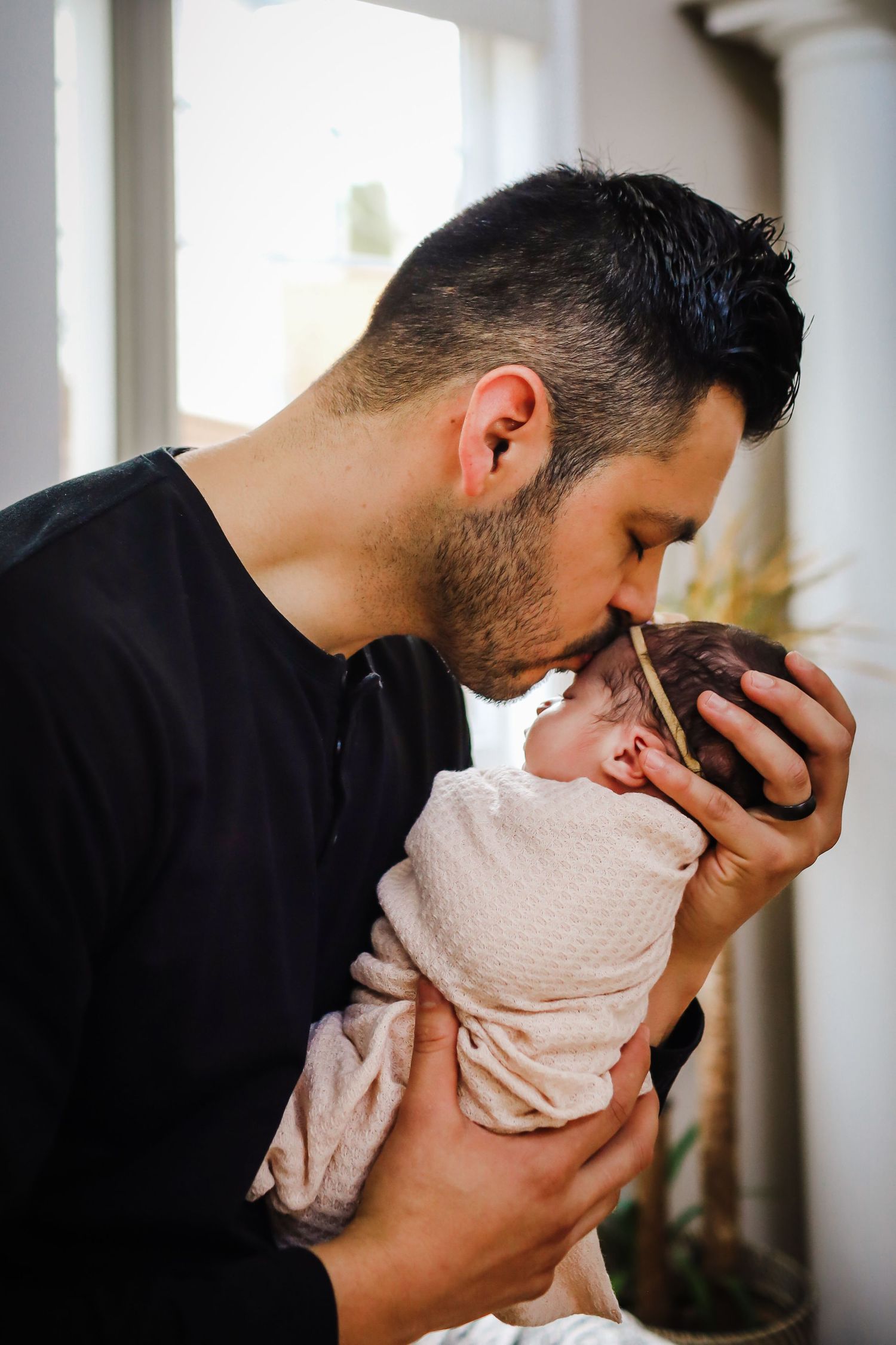 Tender moment between parent and newborn baby wrapped in pink swaddle.