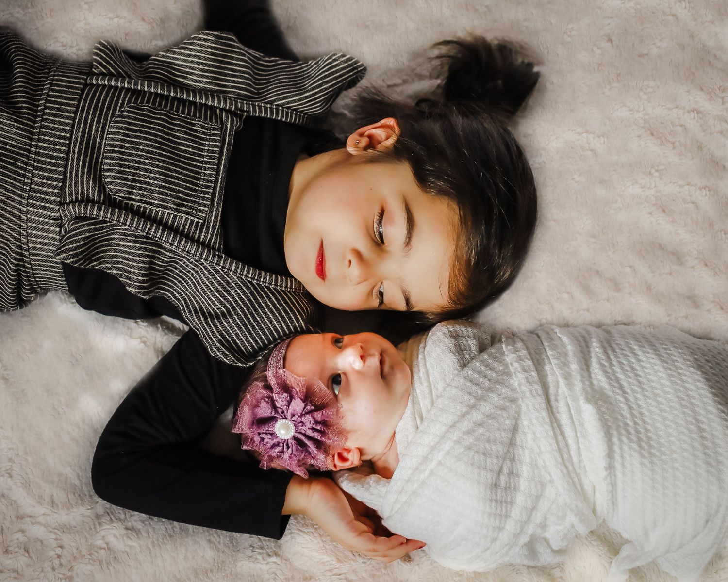 Tender moment of two sleeping babies in grey and white swaddles on soft blanket.