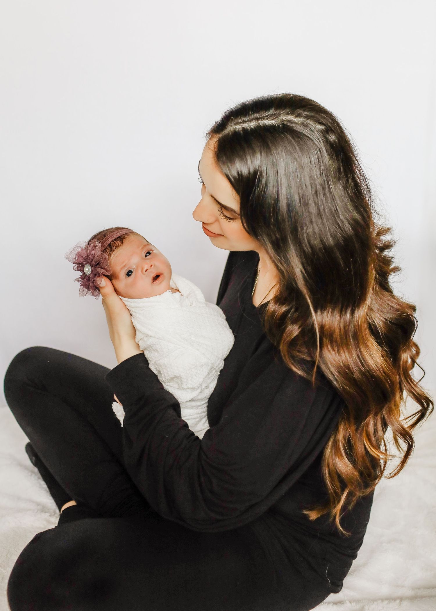 Loving maternal moment with baby wearing floral headband and white swaddle.