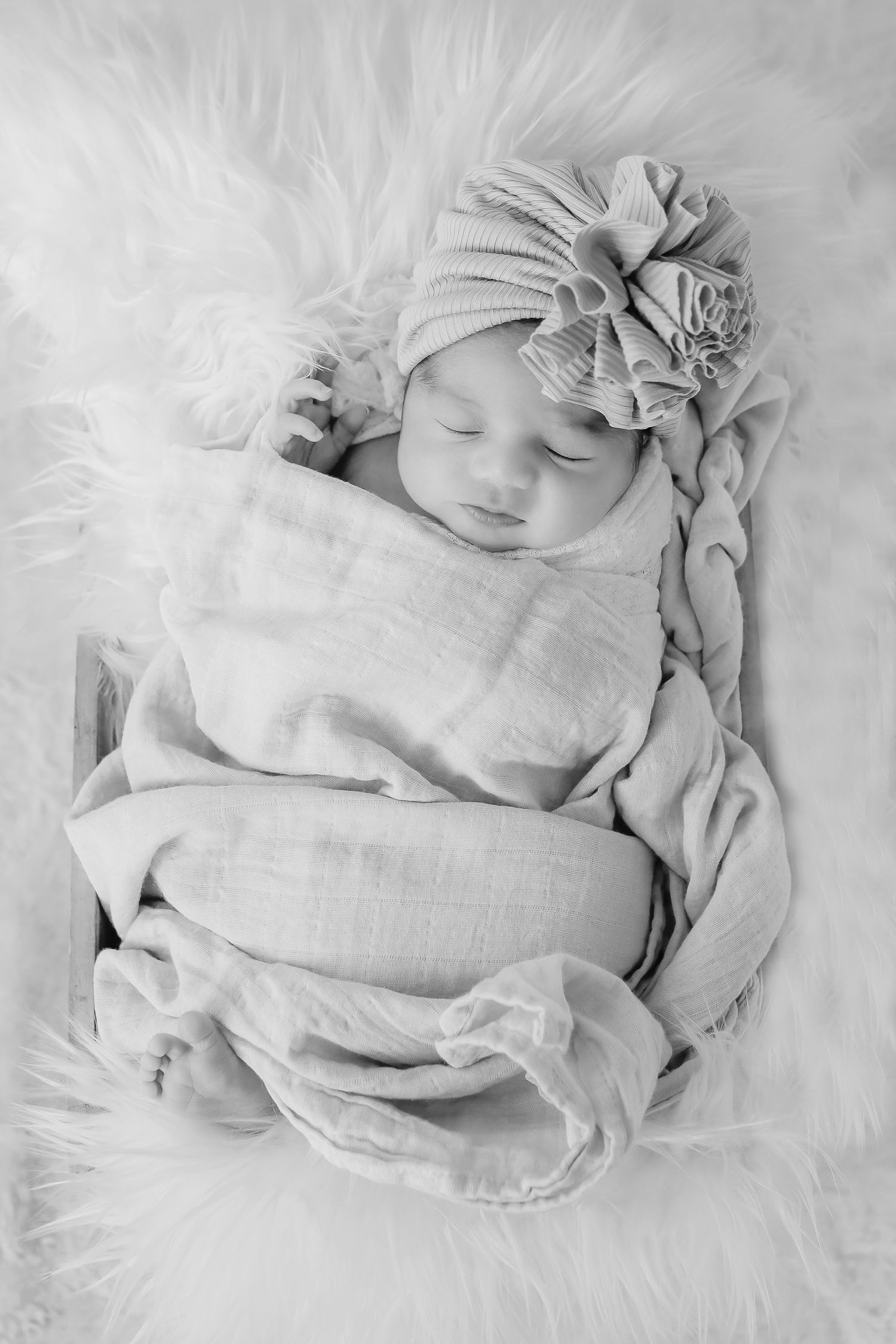 Newborn with grey knit hat sleeping peacefully on white furry blanket in black and white photography.