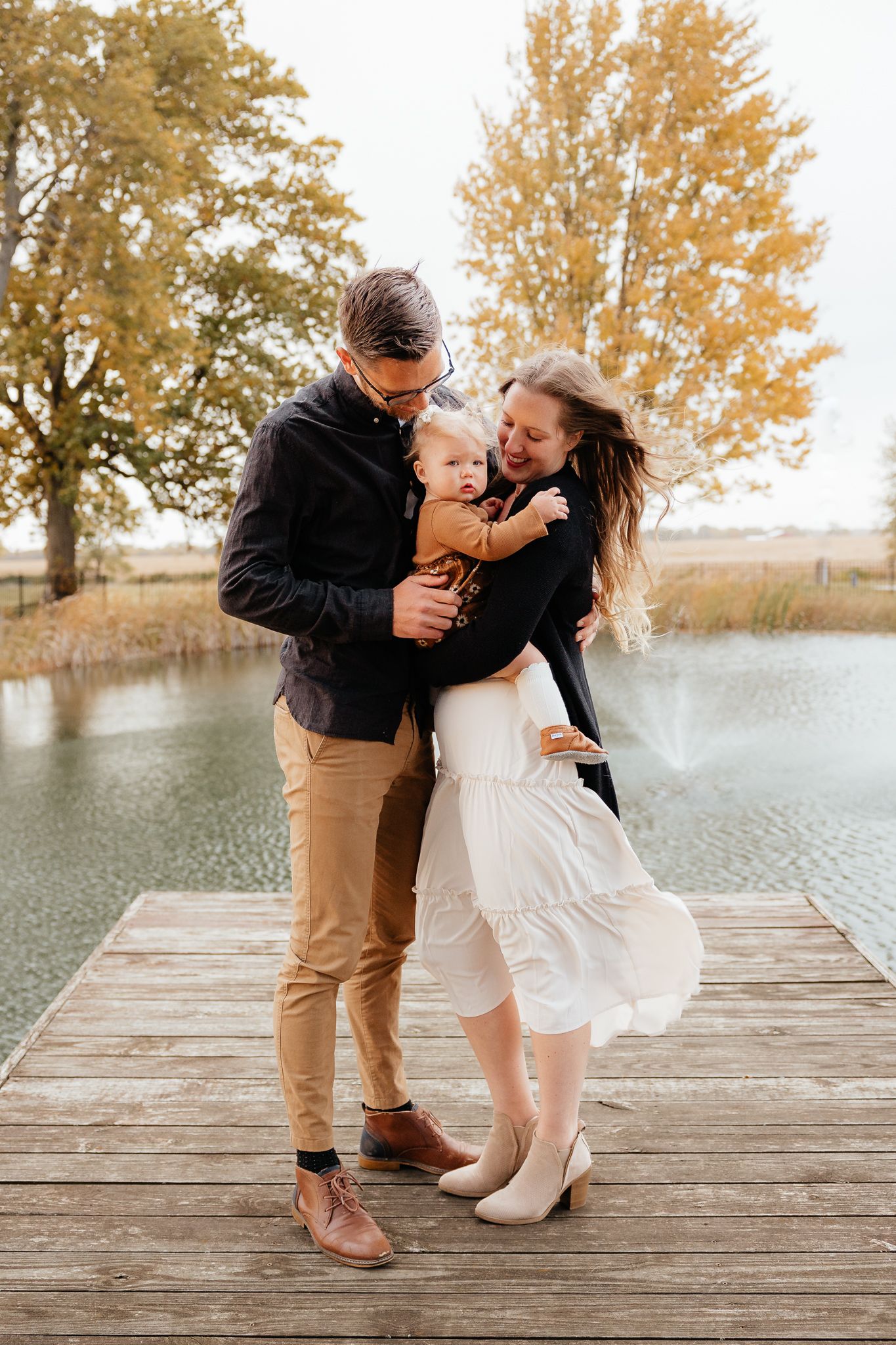 Joyful couple sharing intimate moment on lakeside dock surrounded by fall colors.