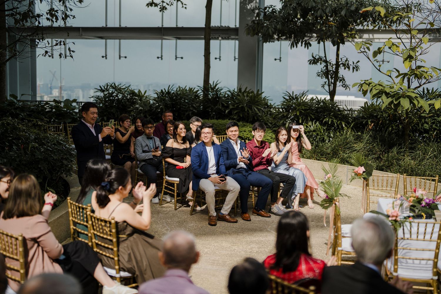 Wedding guests seated outdoors for a garden ceremony with tropical landscaping.