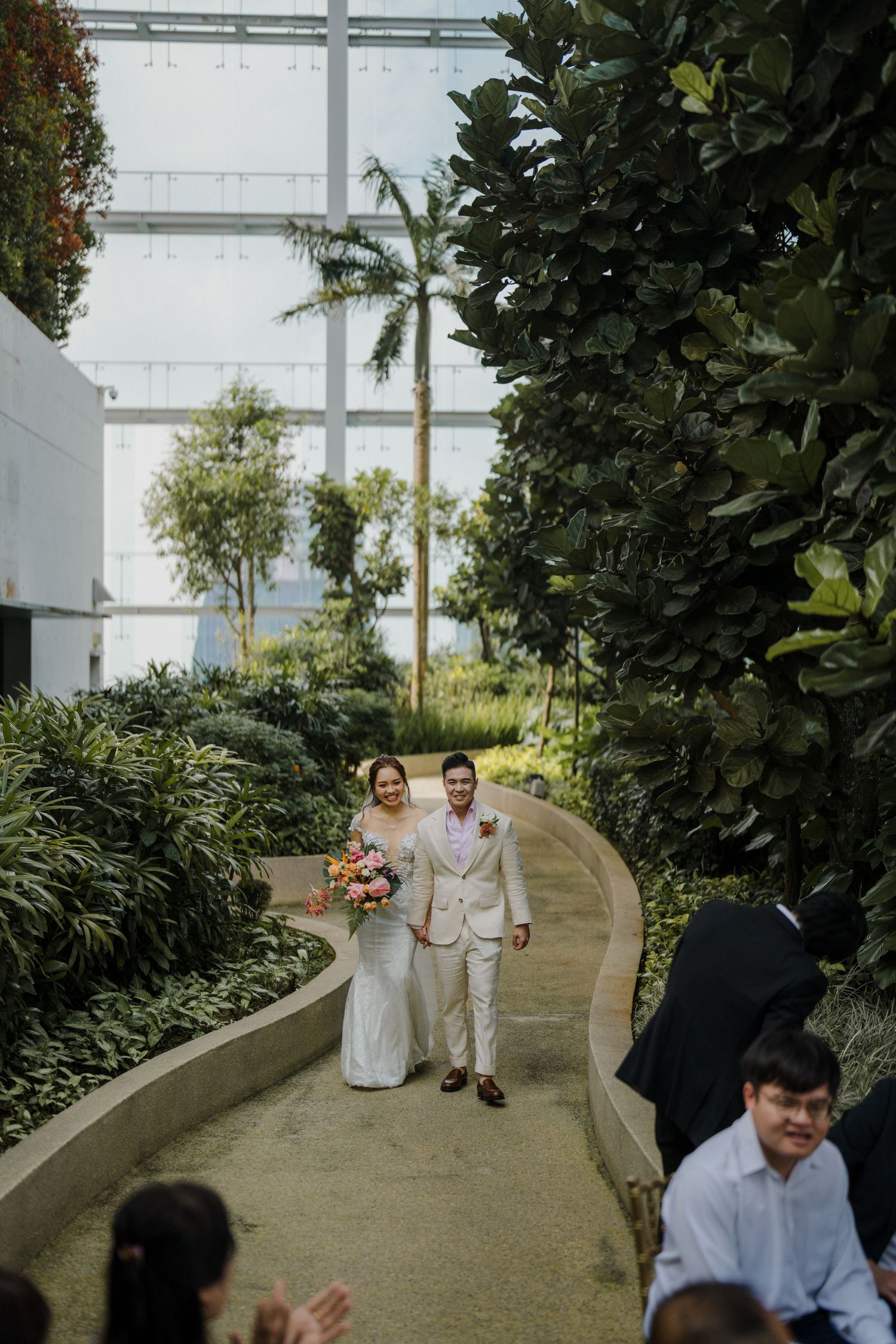 Wedding couple walking down a curved garden path lined with lush greenery.