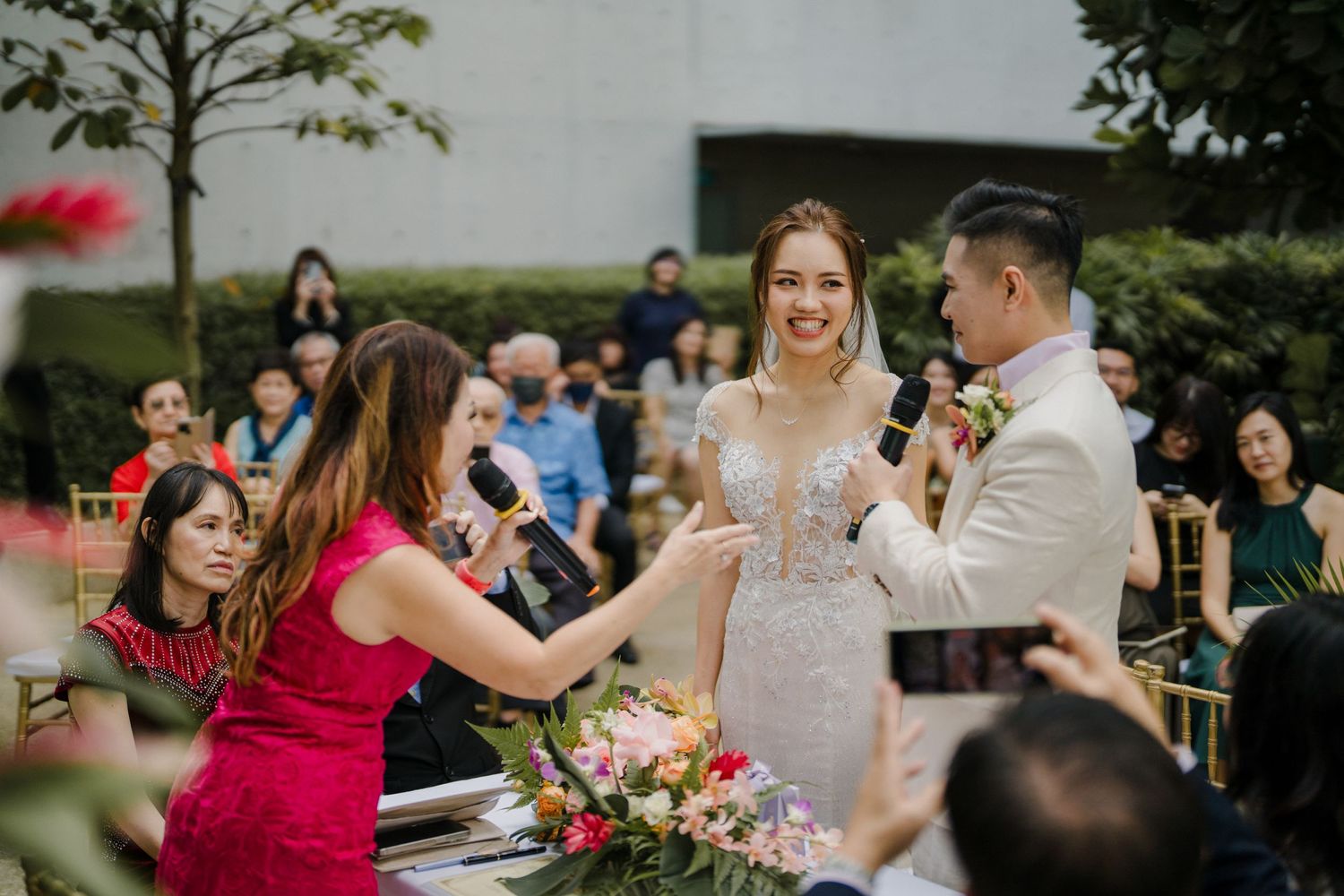 Outdoor wedding celebration with guests in formal attire and bright pink floral arrangements.
