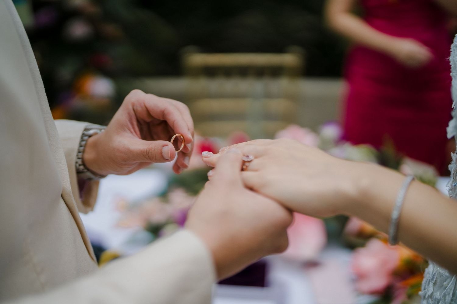 Close-up of hands during wedding ring exchange ceremony outdoors.