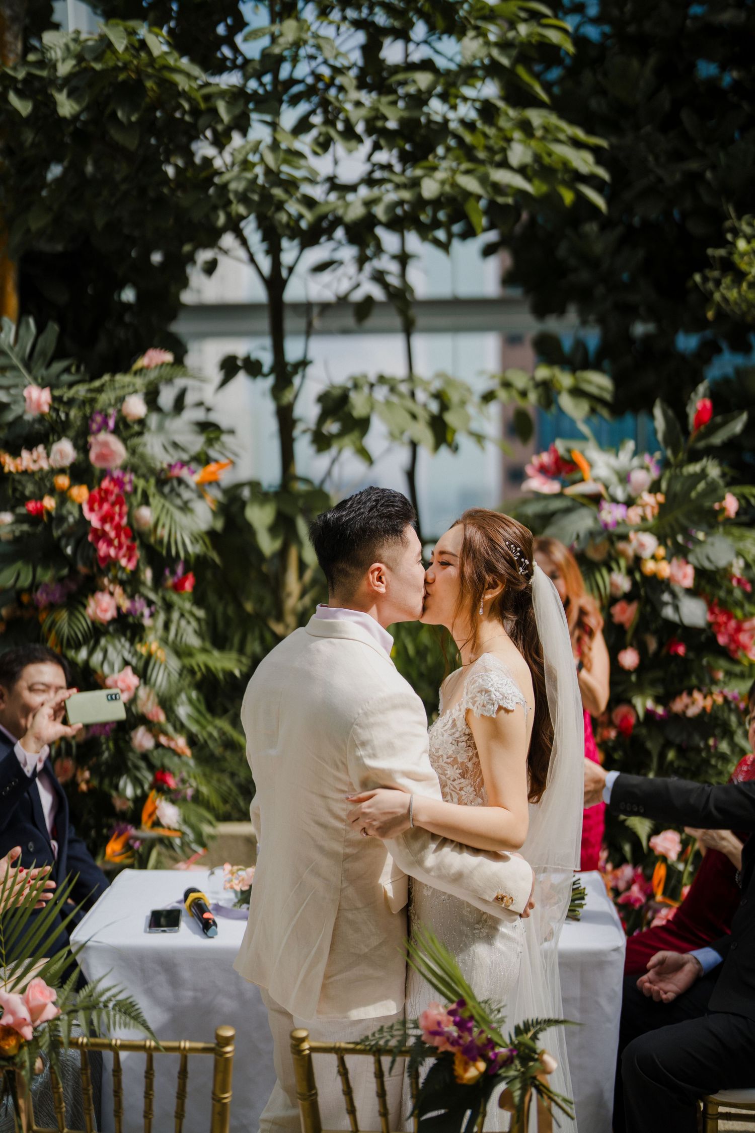 Newlyweds share their first kiss at garden ceremony with floral backdrop.
