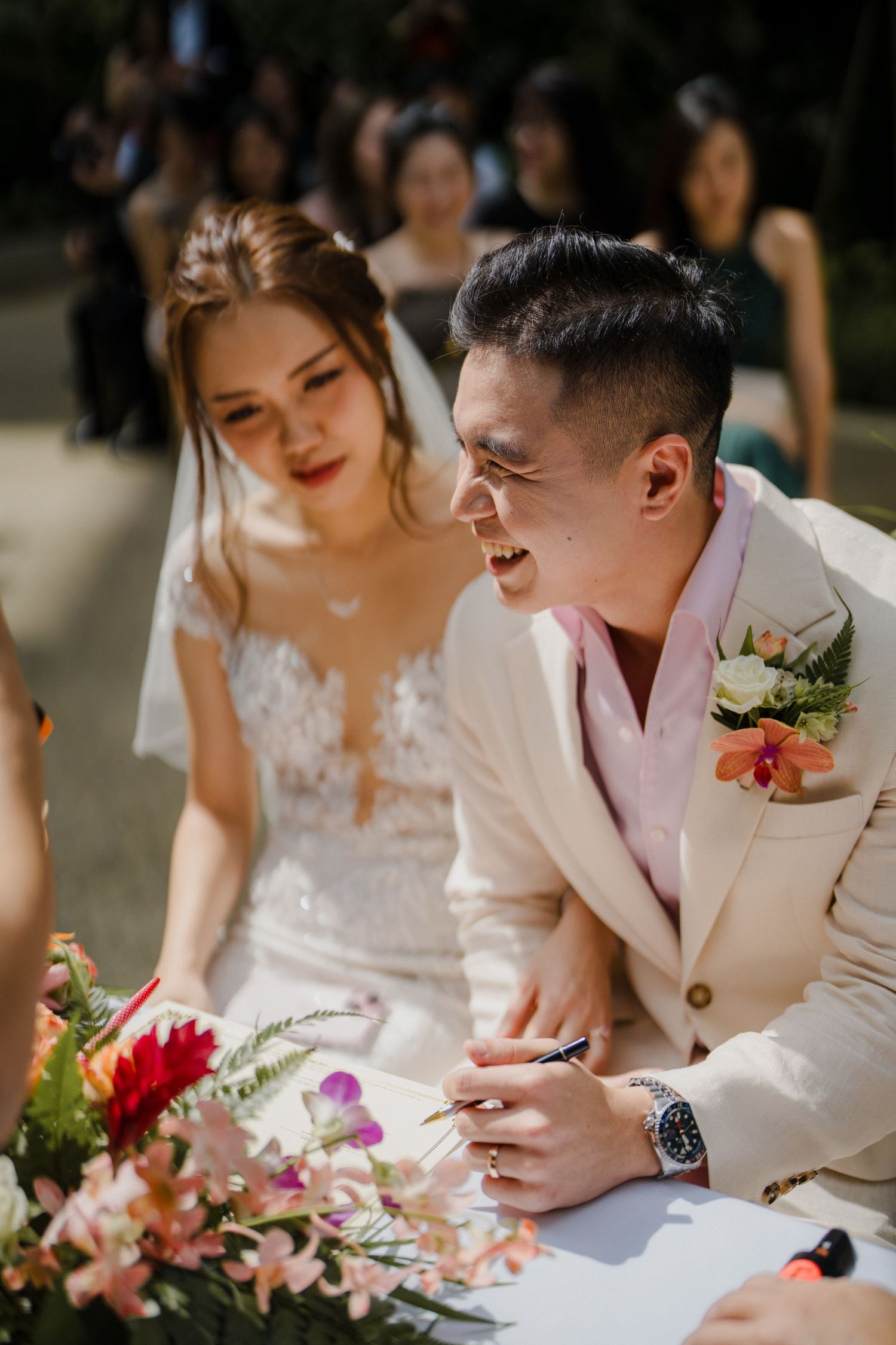 Couple signing wedding documents together with colorful floral arrangements on the table.