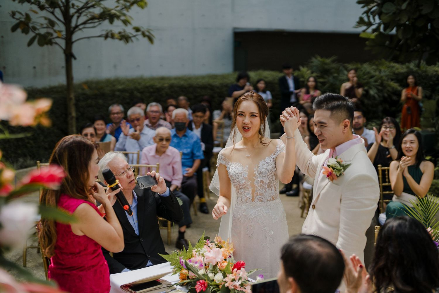Wedding ceremony guests gathered outdoors with floral decorations.