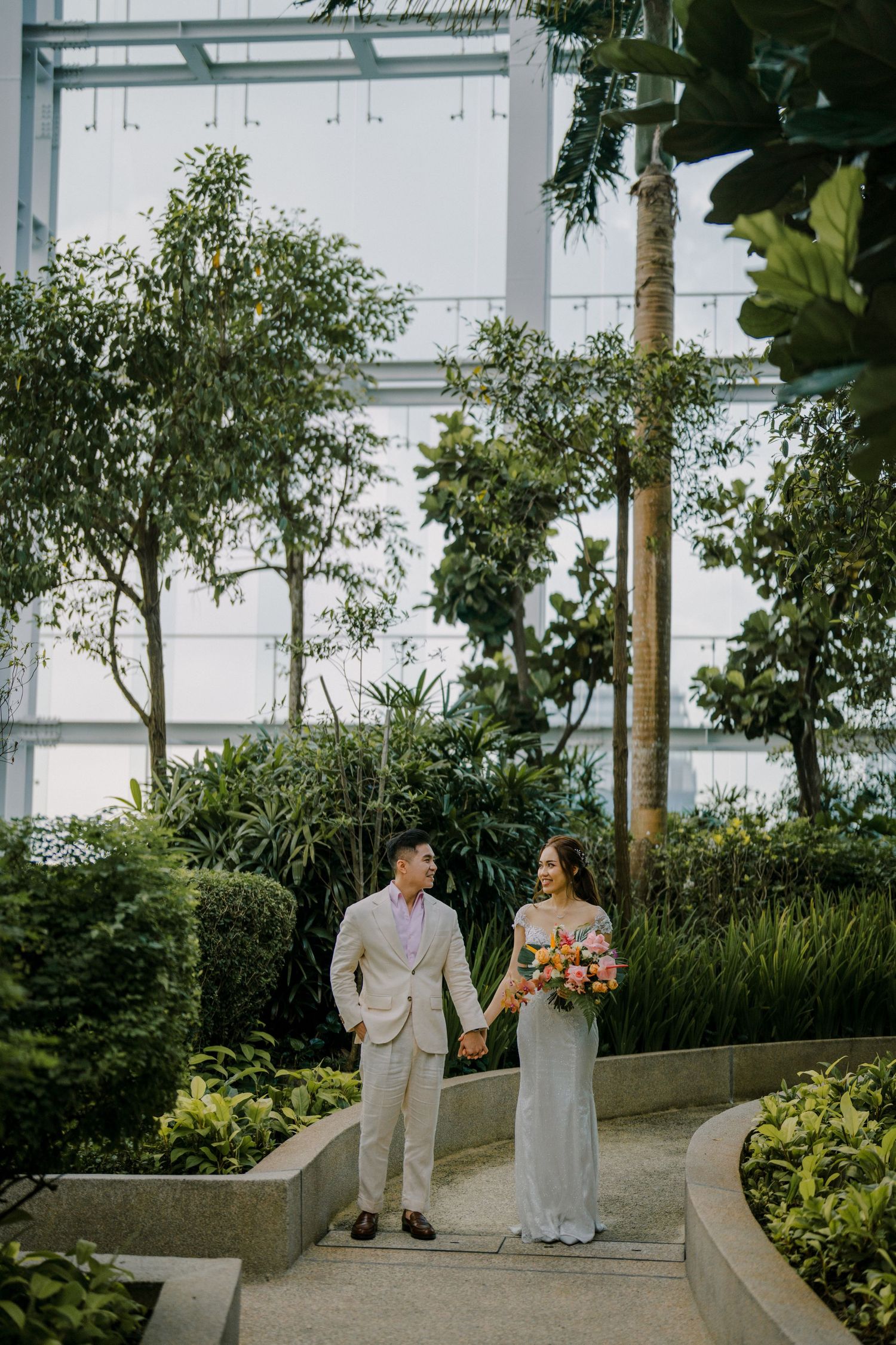 A couple walks along a curved garden path surrounded by lush tropical plants.