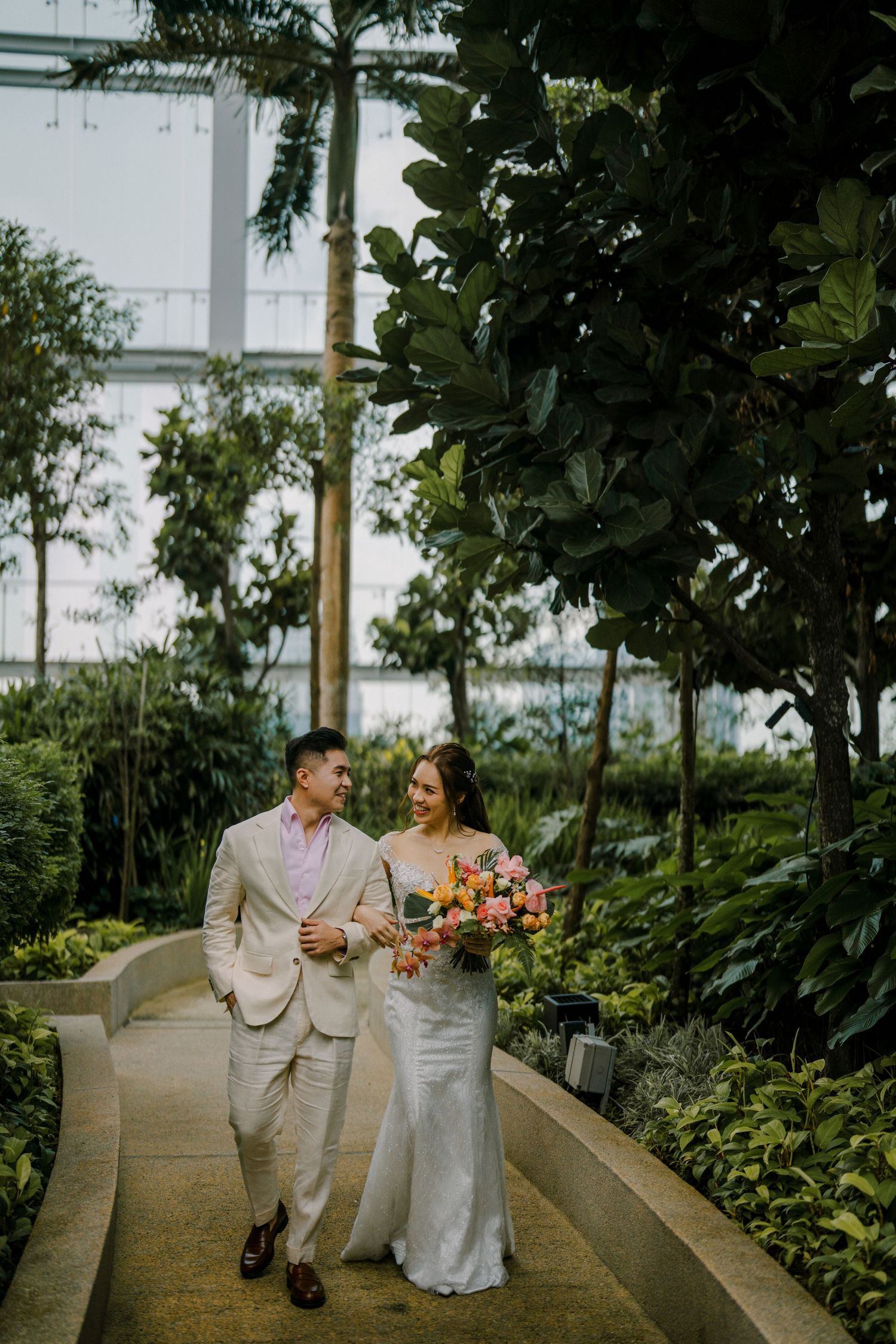 A couple in light colored attire strolls through a modern garden setting.