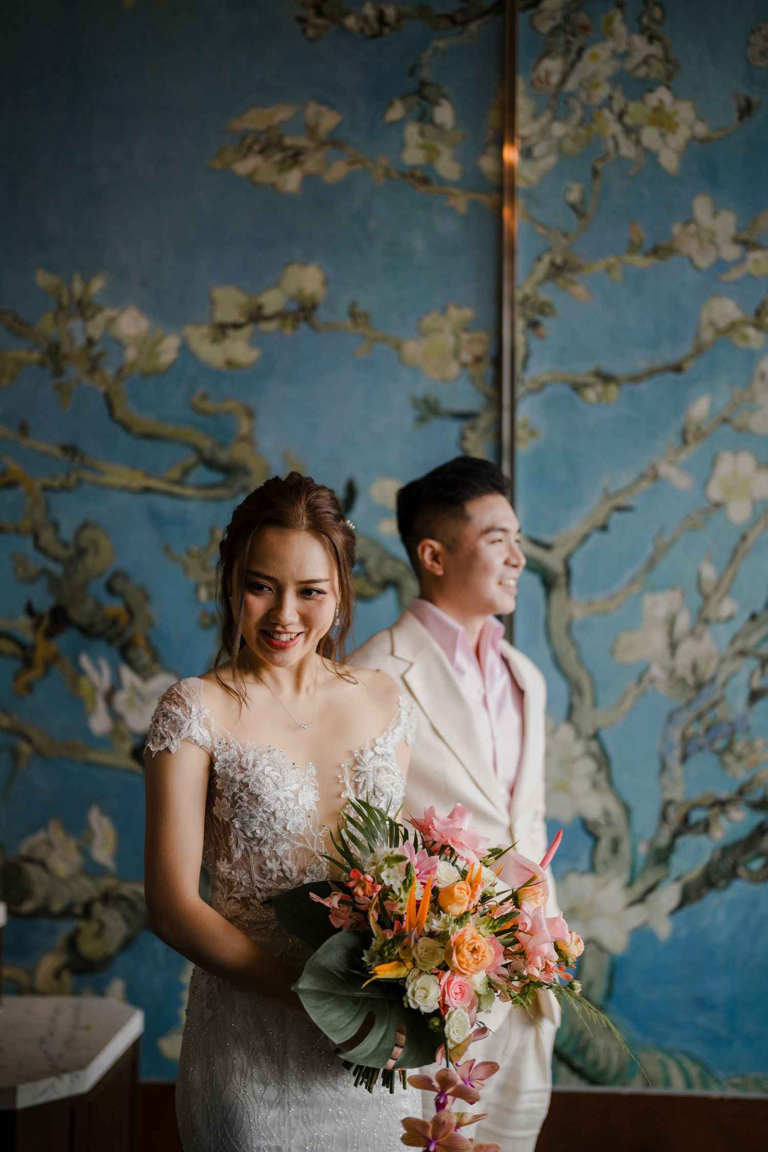 A wedding couple poses against a blue floral backdrop in an elegant indoor setting.