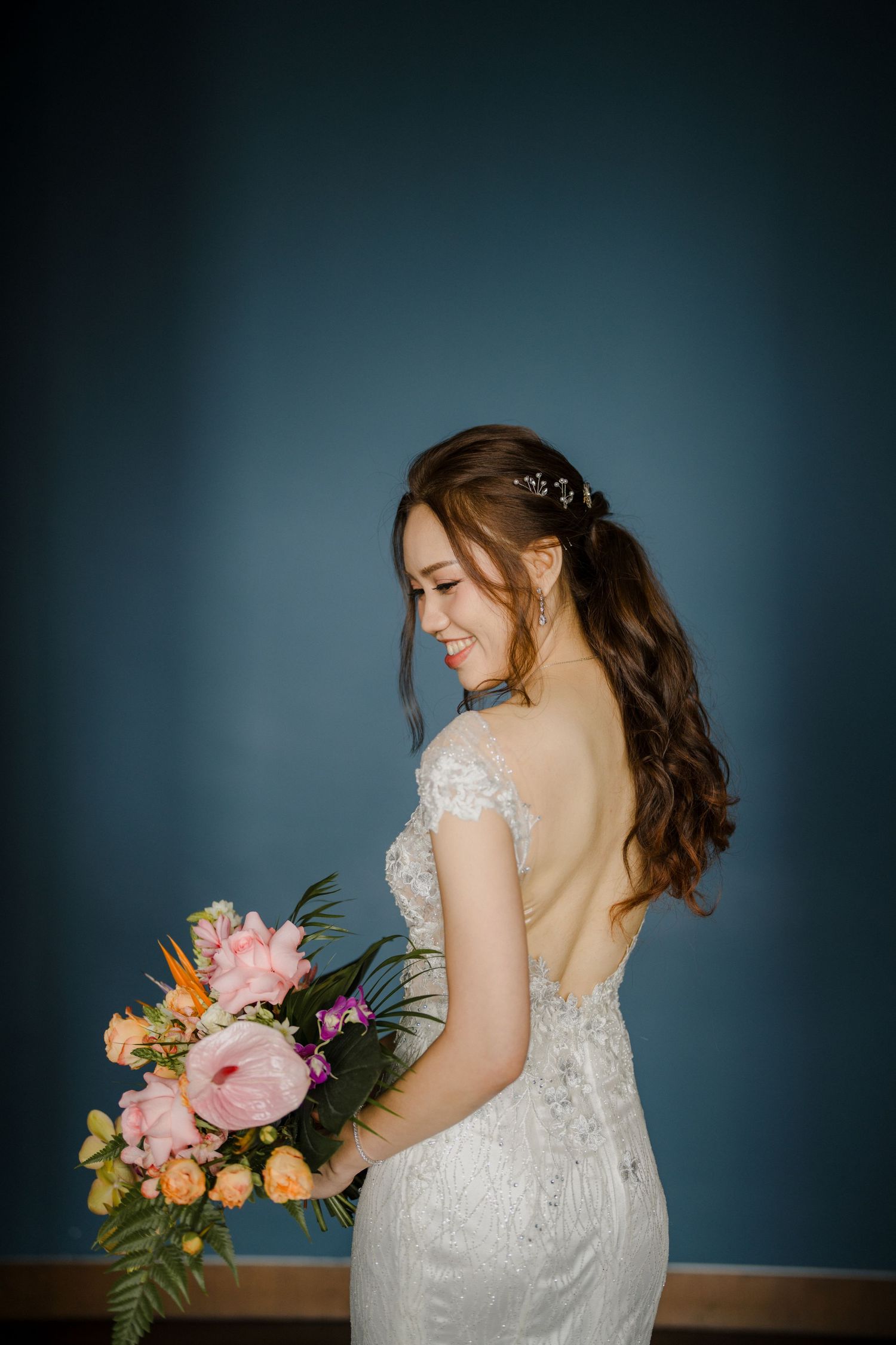Side profile of a bride in a lace wedding dress holding a colorful bouquet.