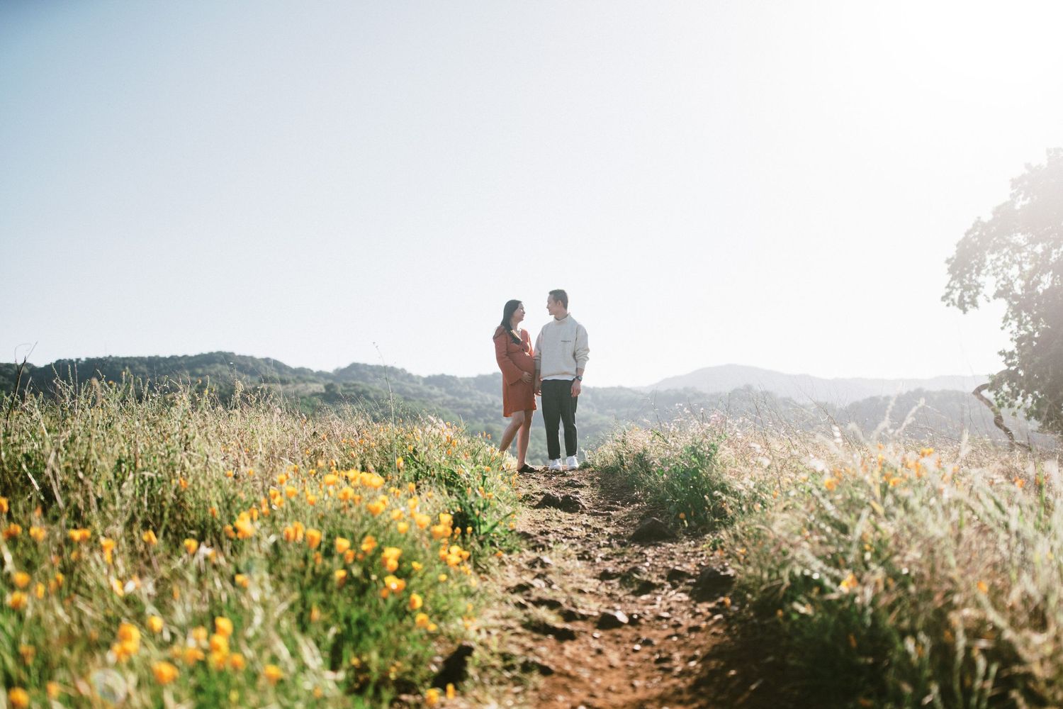 Two people stand on a hilltop trail surrounded by wildflowers at golden hour.