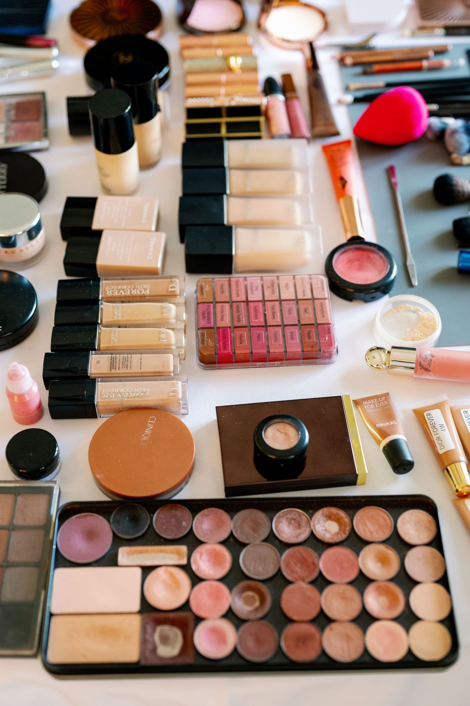 Extensive collection of makeup products and cosmetics arranged on white surface.