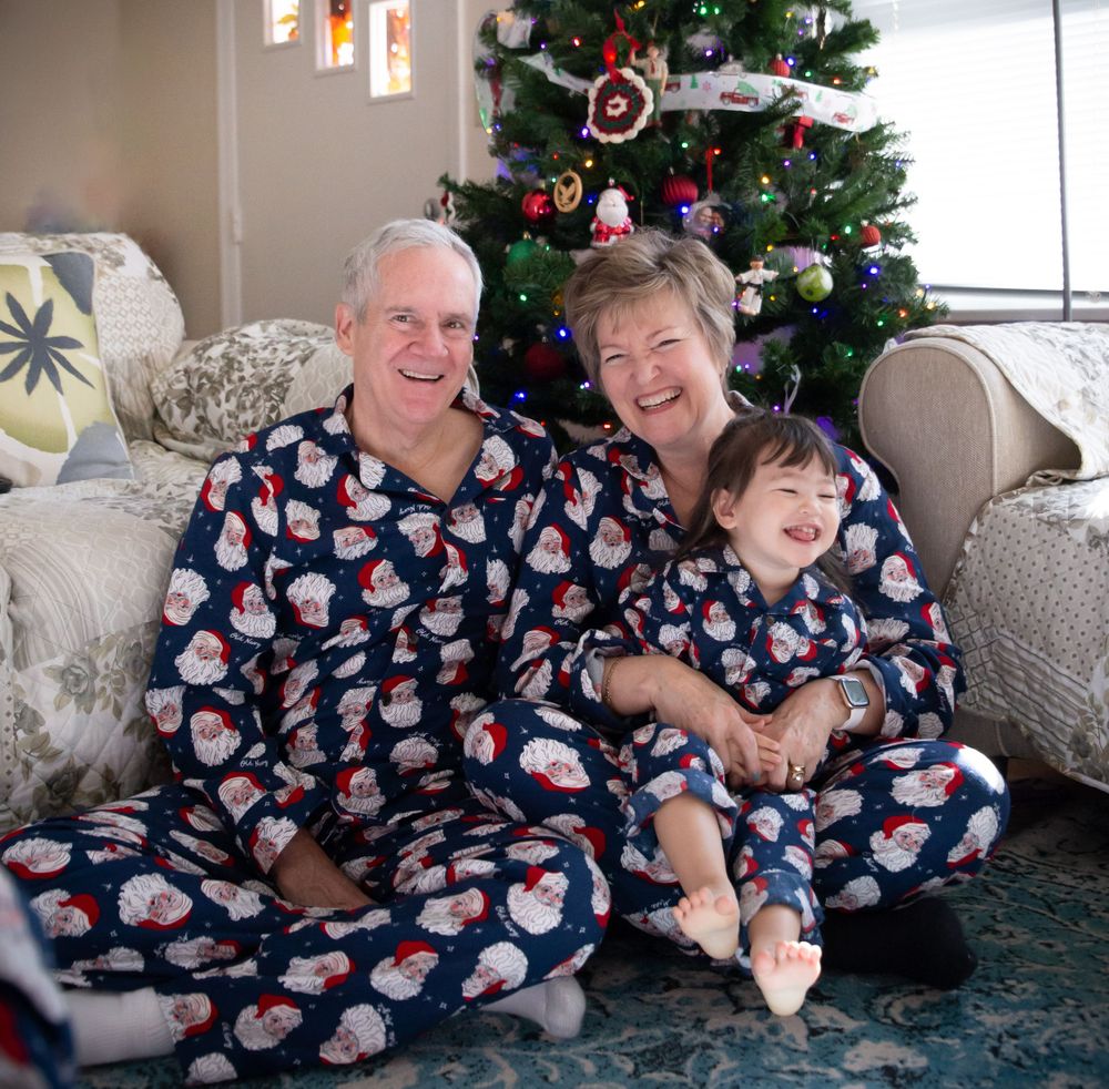 Family wearing matching Santa pajamas posing in front of Christmas tree.