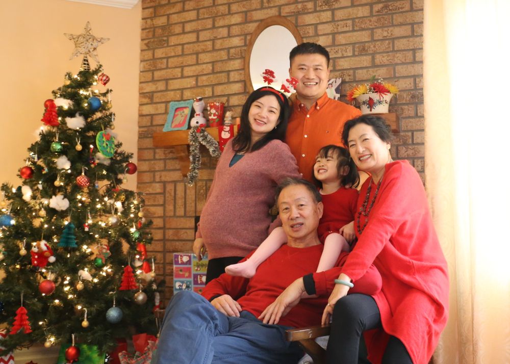 Family gathered around Christmas tree in living room with brick fireplace.