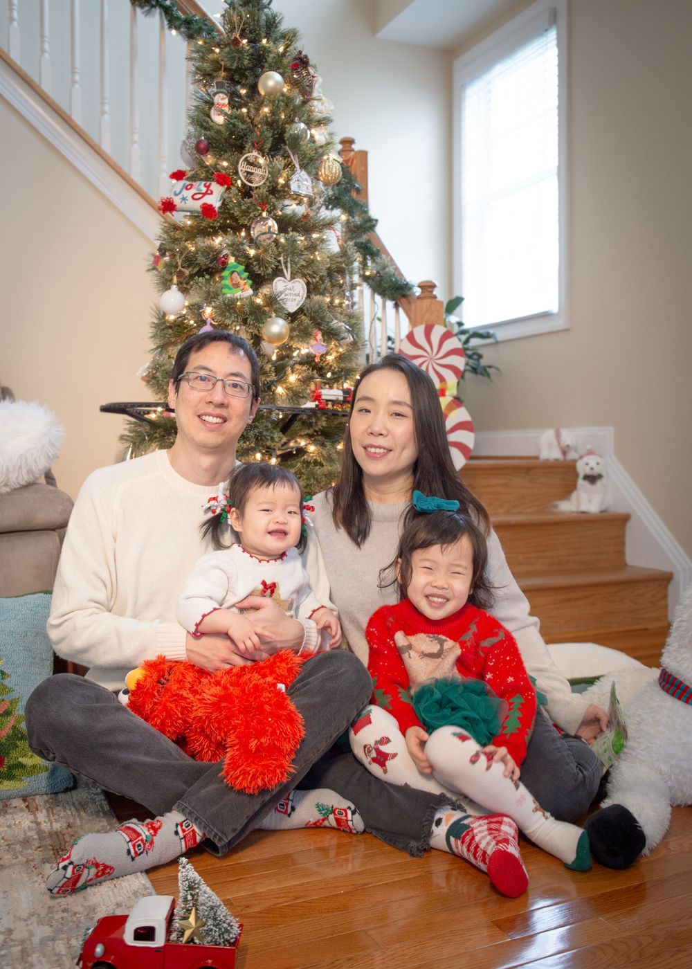 A festive family photo in front of a decorated Christmas tree with matching holiday pajamas and seasonal decor.