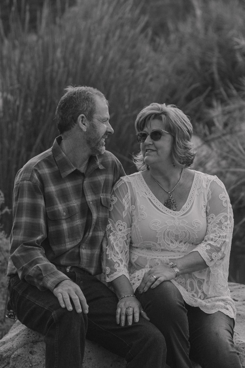 A black and white portrait of a couple sitting together outdoors in casual attire.