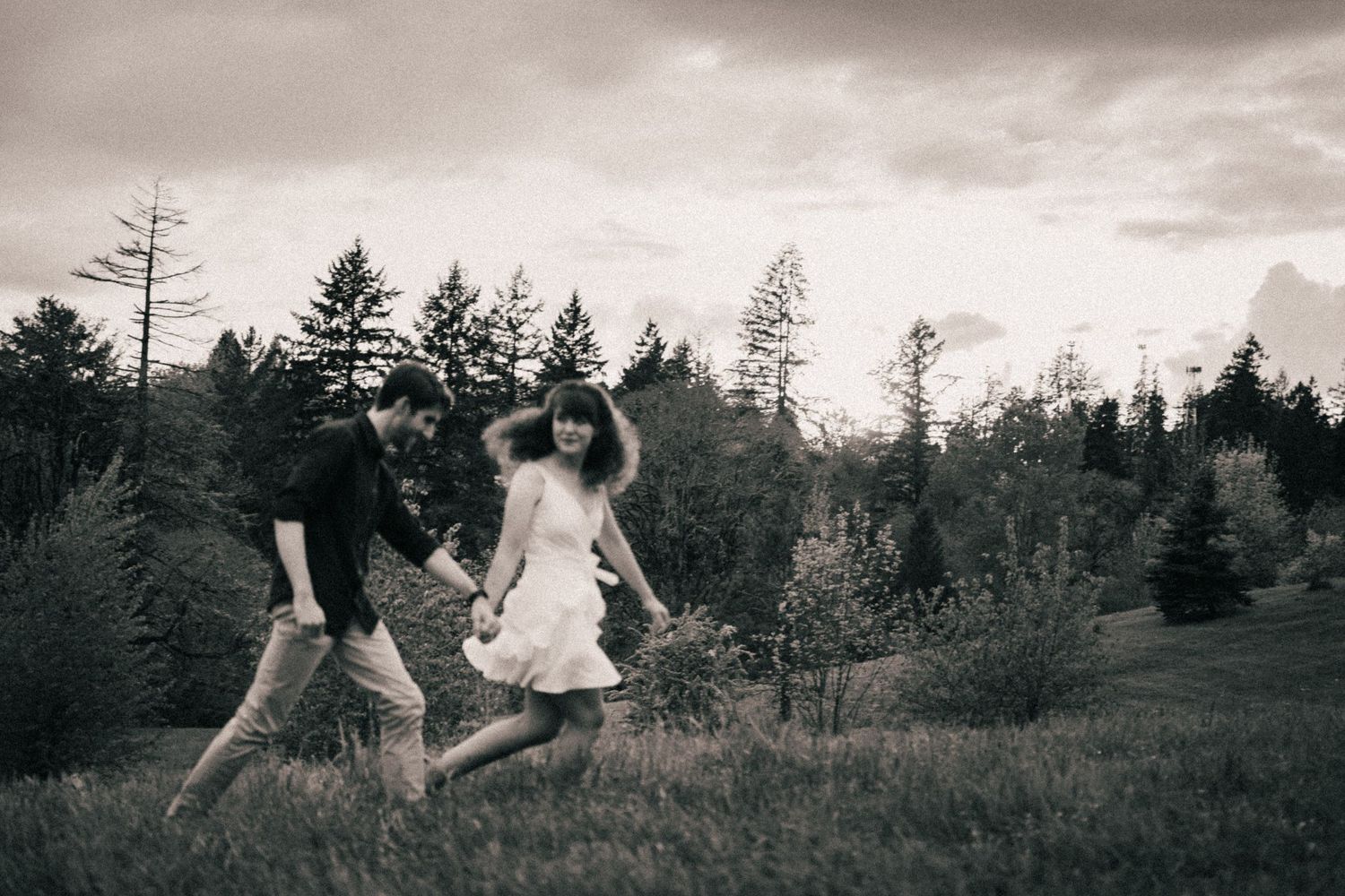 Black and white photo of someone twirling in a dress against a moody forest backdrop.