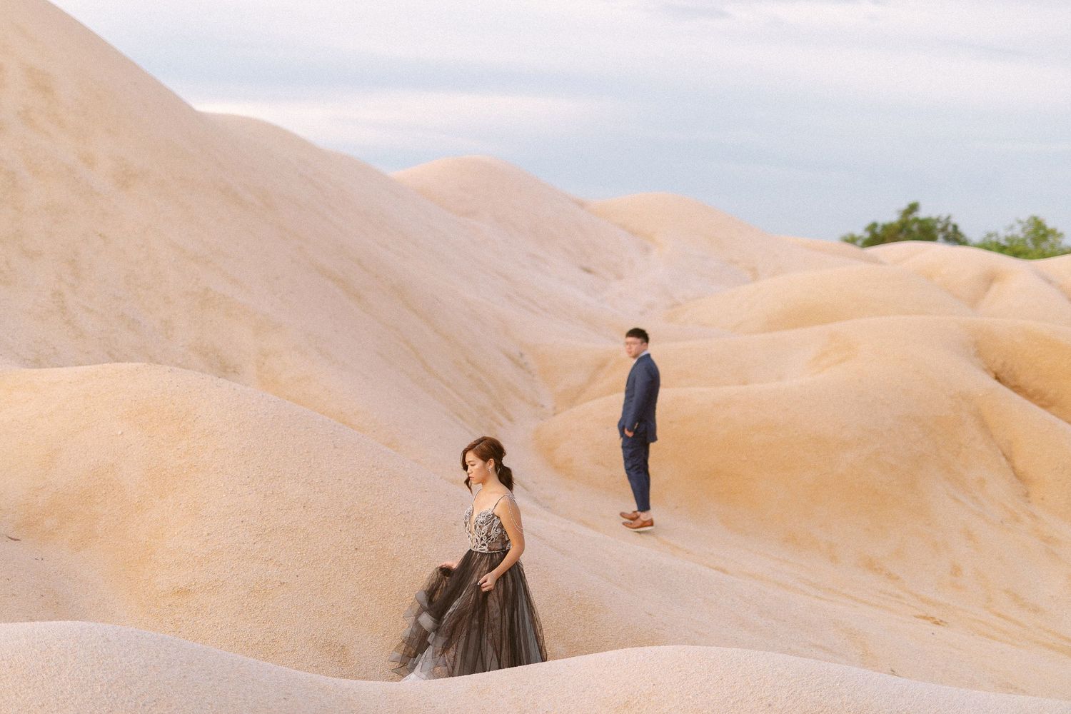 Couple walking through scenic sand dunes during a sunset photoshoot in a desert landscape.