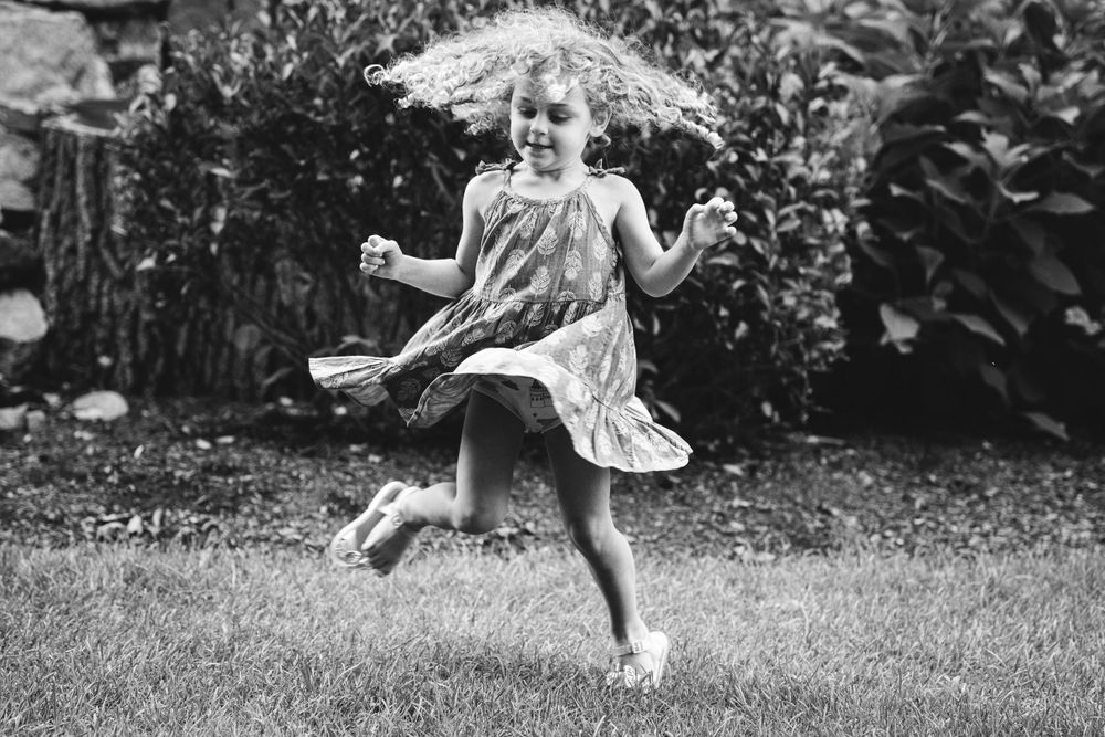 Black and white photo of young child dancing joyfully in garden.