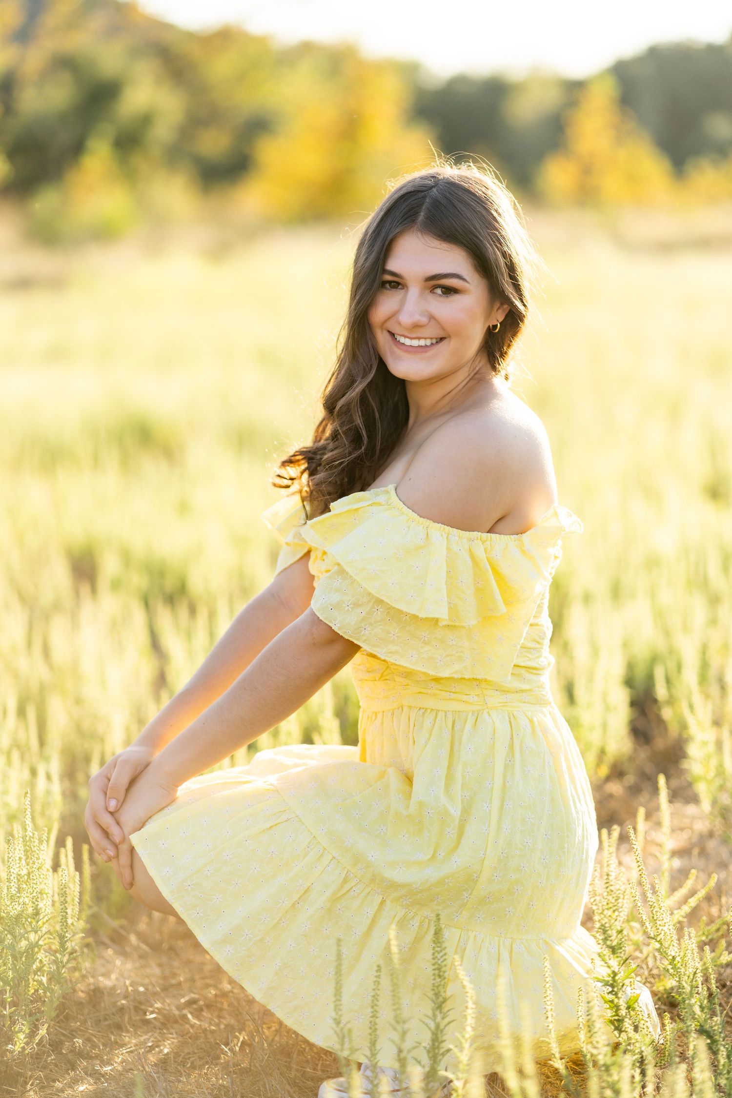 A high school senior in yellow ruffled sundress posing in golden meadow at sunset.