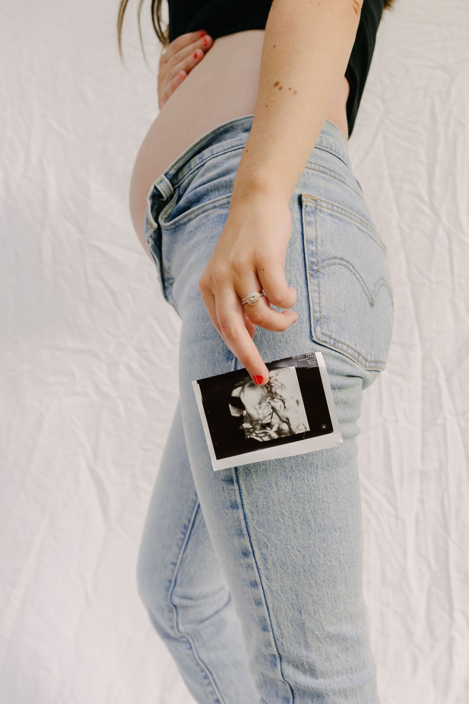 Person in light jeans holding a mobile phone against their back pocket.