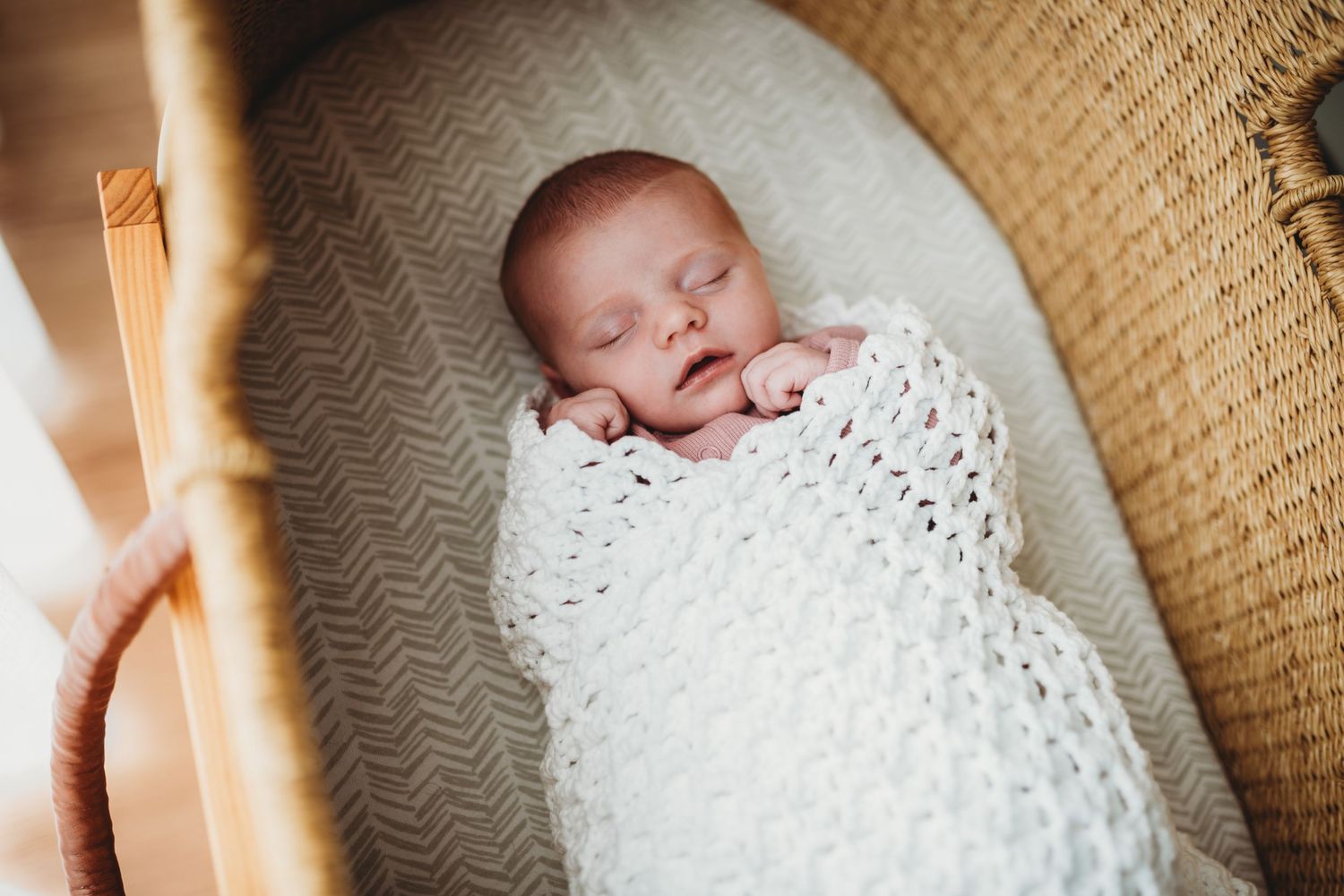 Sleeping newborn wrapped in white knit blanket in woven basket.