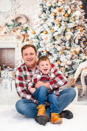 A festive holiday scene with matching plaid shirts in front of a decorated white Christmas tree with wrapped presents.