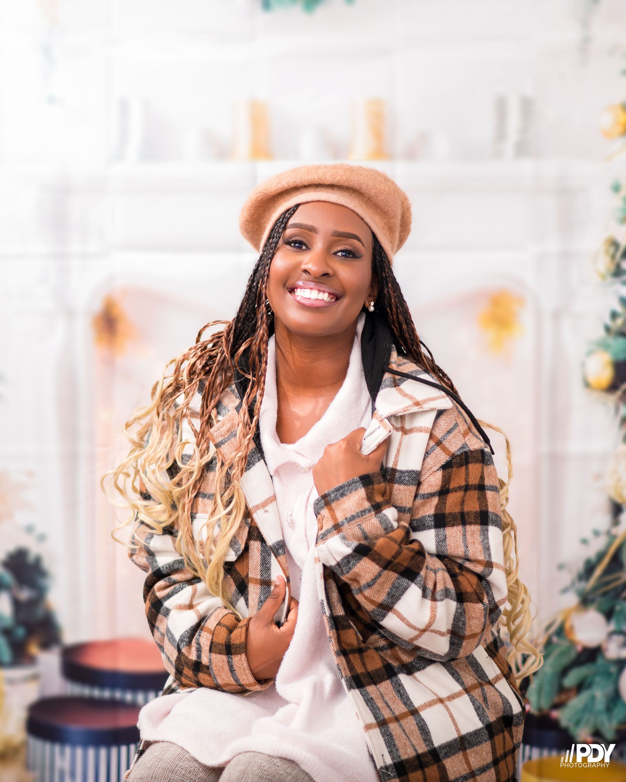 Cozy winter fashion shoot with plaid coat and beret against holiday decorations.