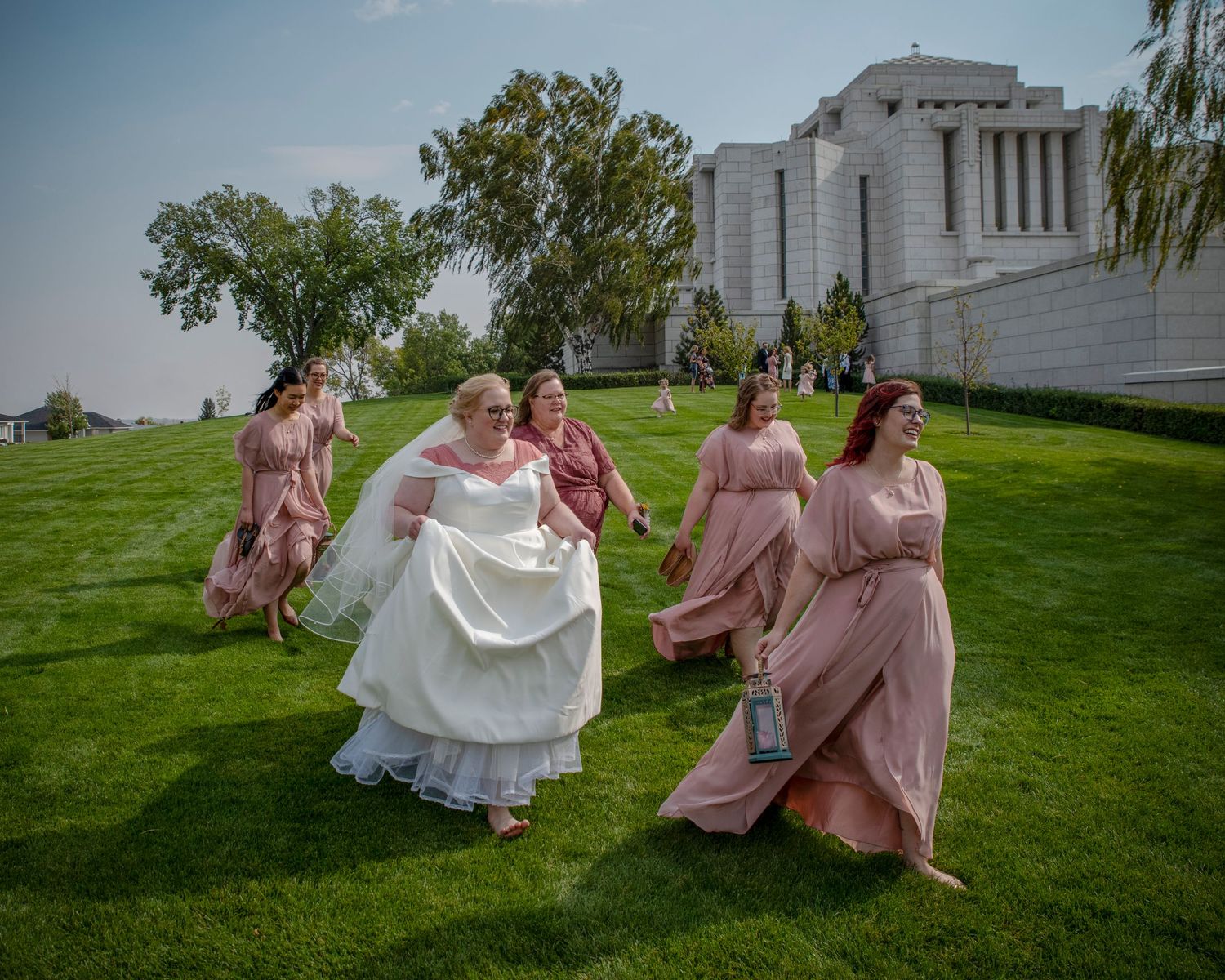 Wedding party in motion on green lawn near classical architecture.
