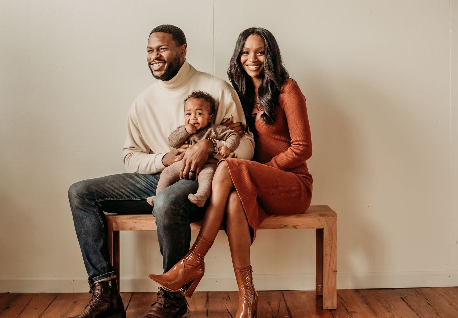 Happy Black family with toddler poses on wooden bench in warm earth-toned outfits.