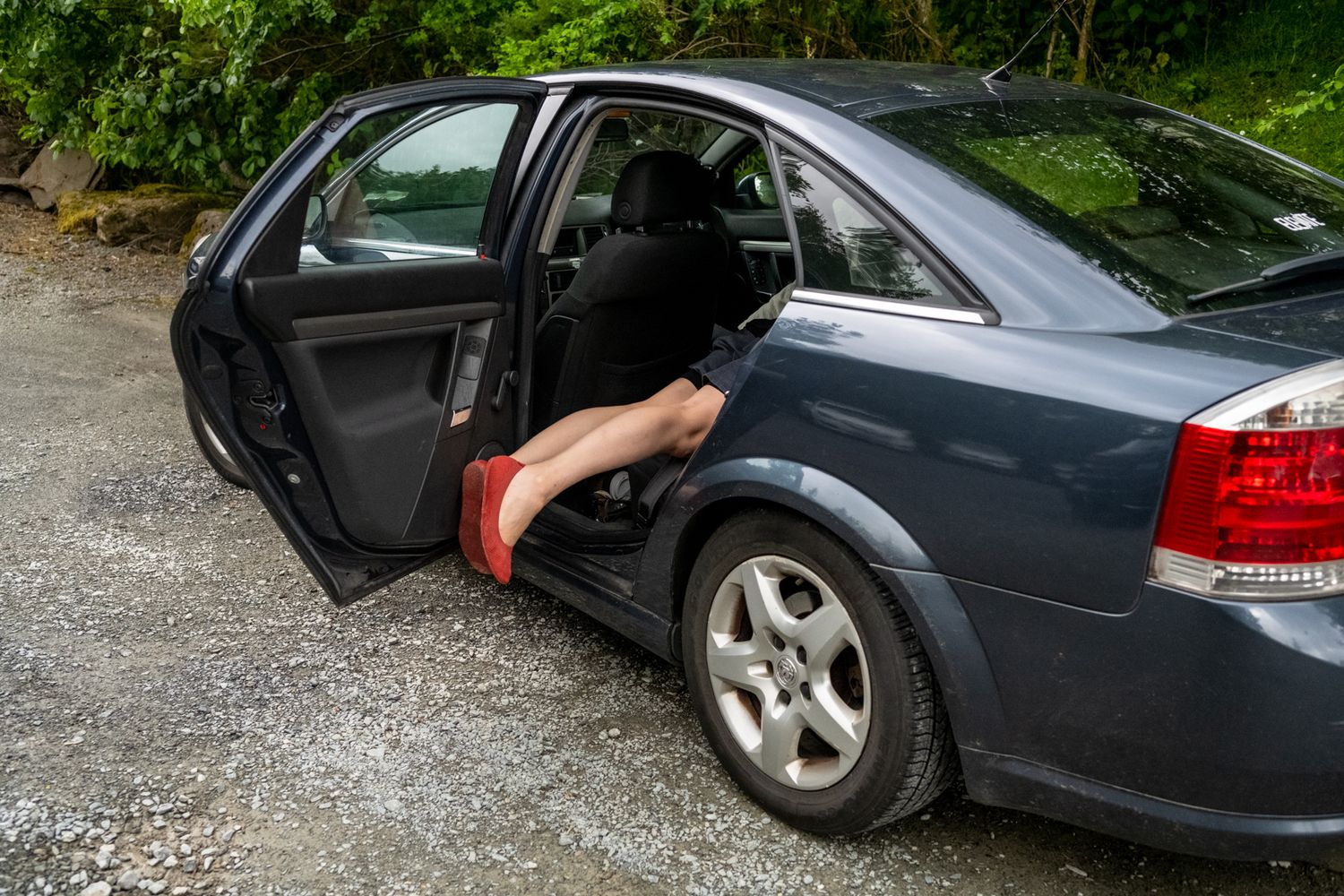A foot in formal shoes steps out of a dark grey sedan car.