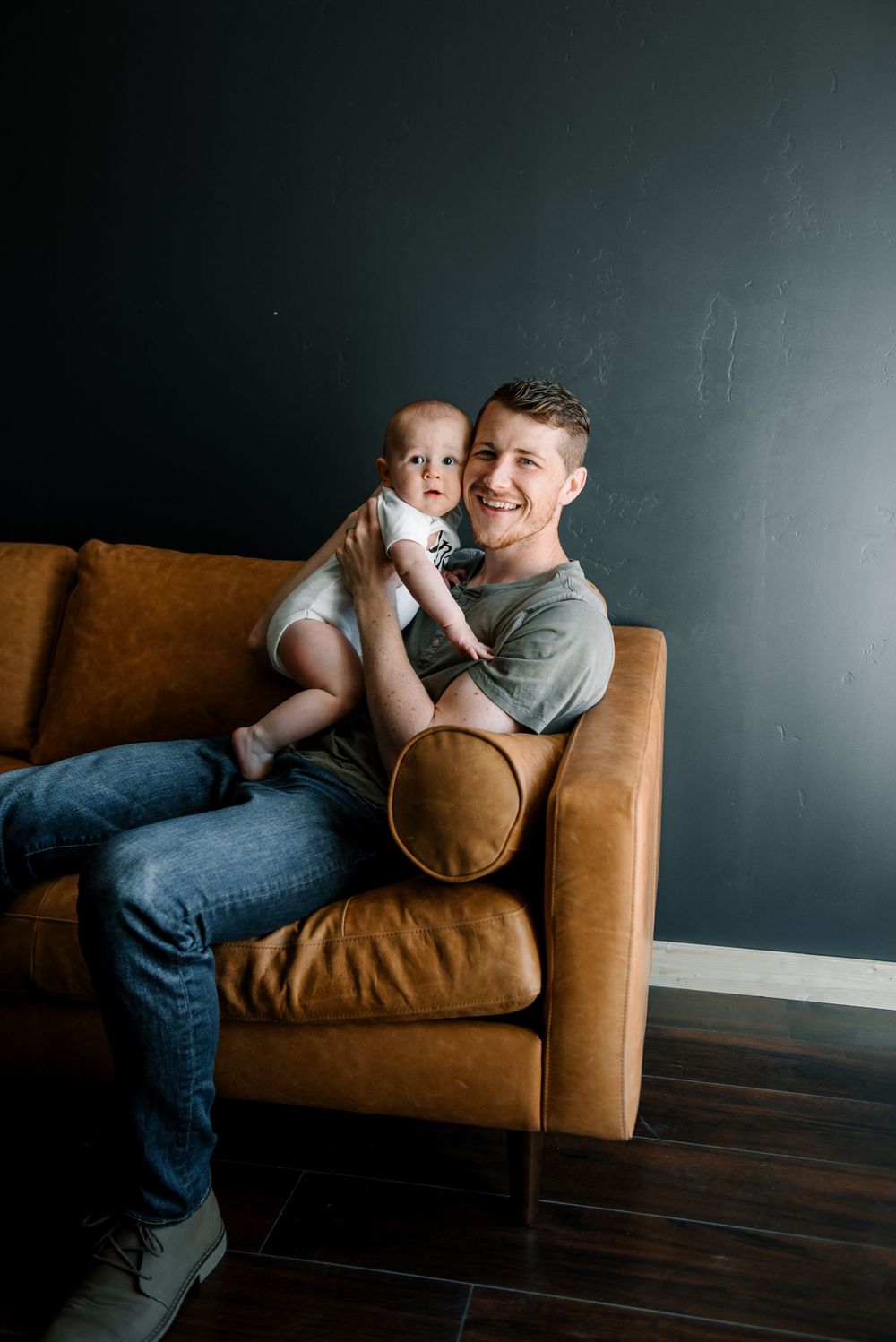 Candid moment of parent and baby laughing together on brown leather couch.