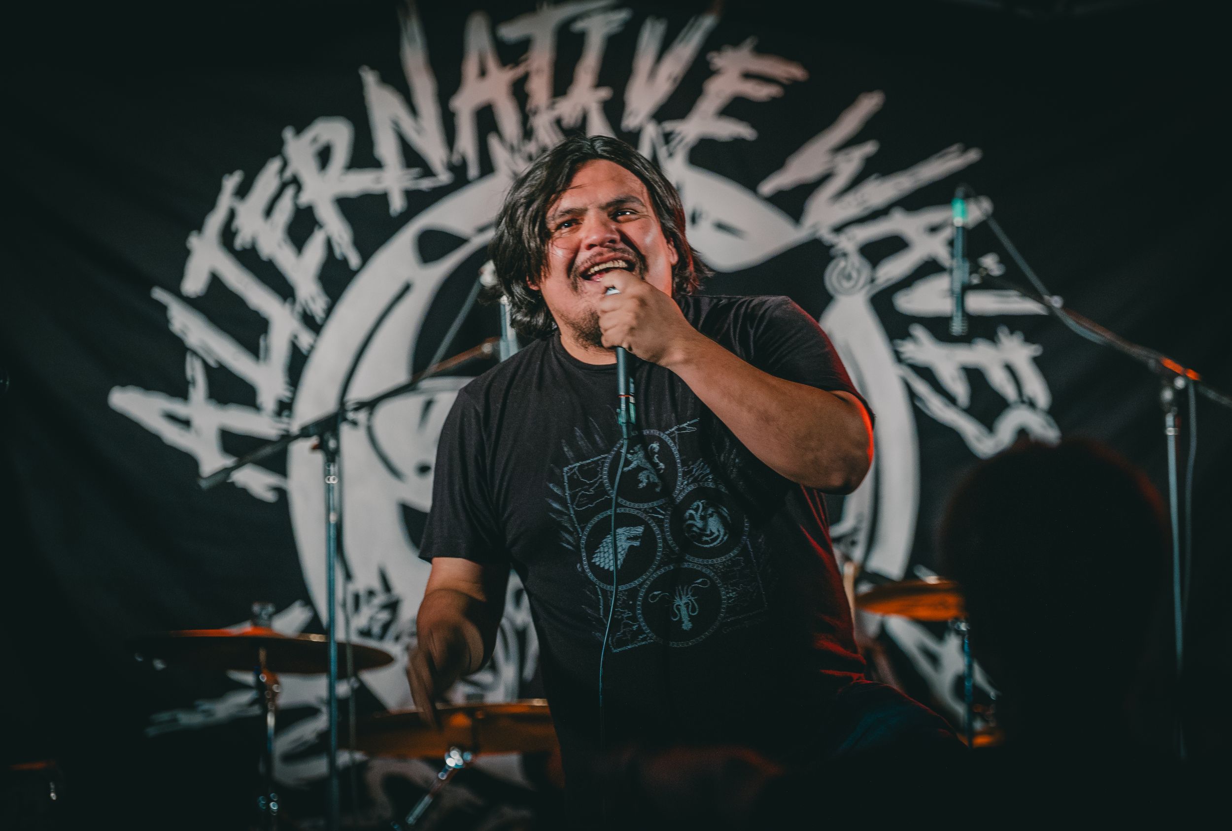 Energetic performer singing on stage with Alternative Music text display behind.