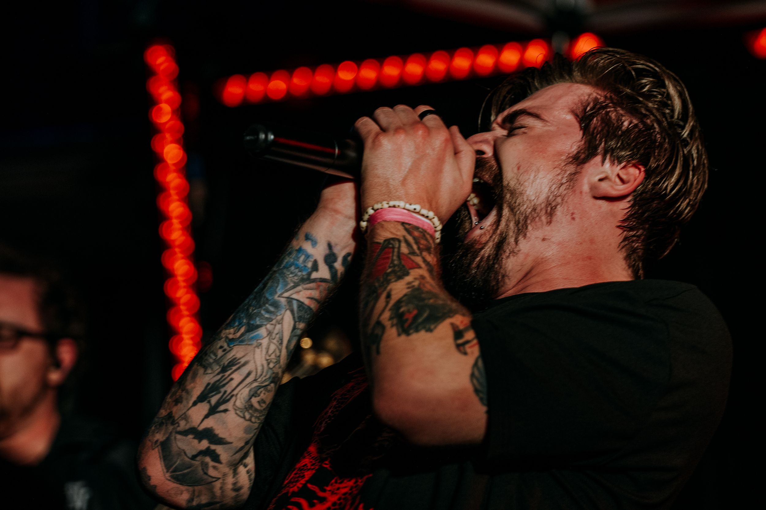 Passionate singer performing intensely with tattoos and red lighting.