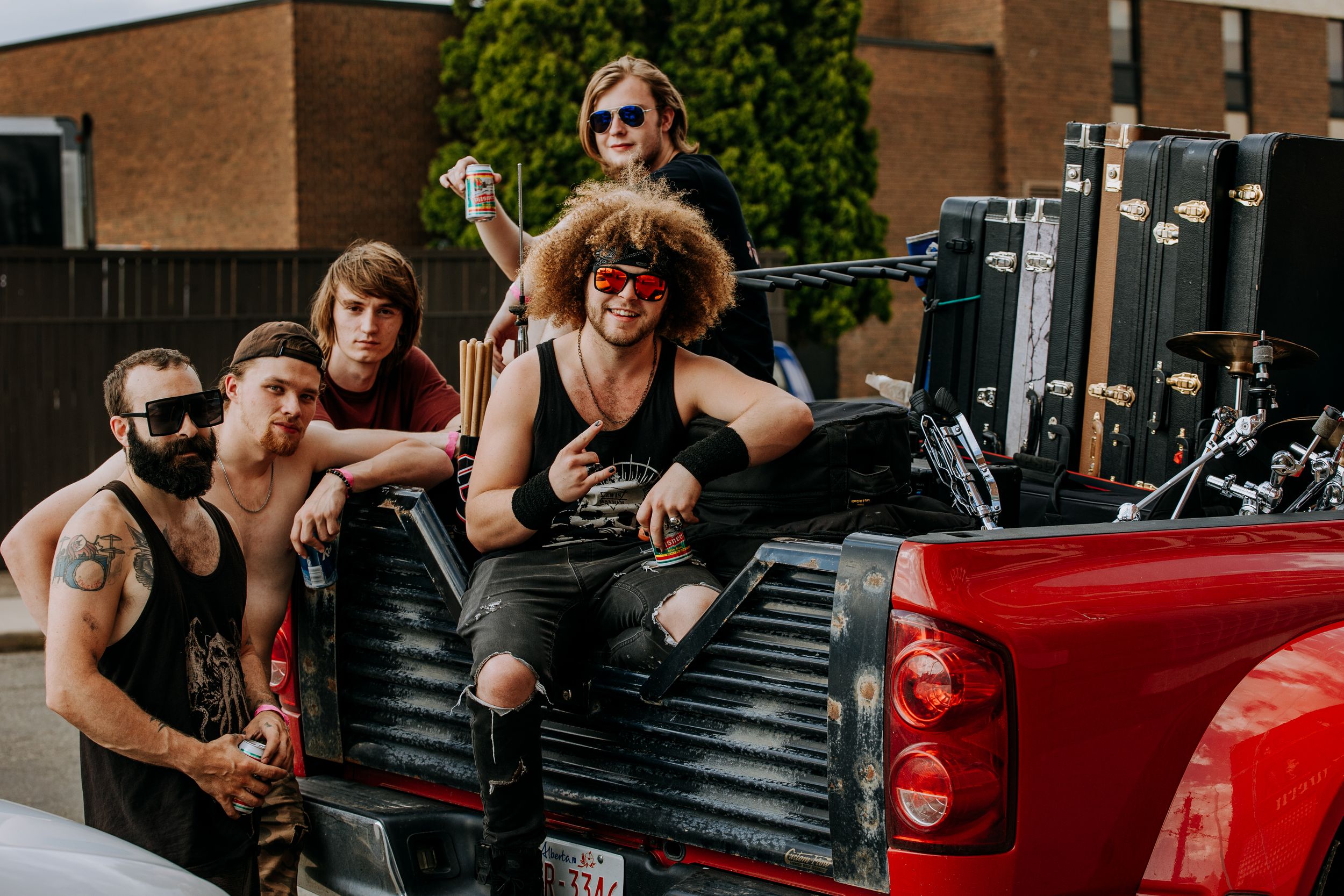 Musicians posing together in the back of a red pickup truck.