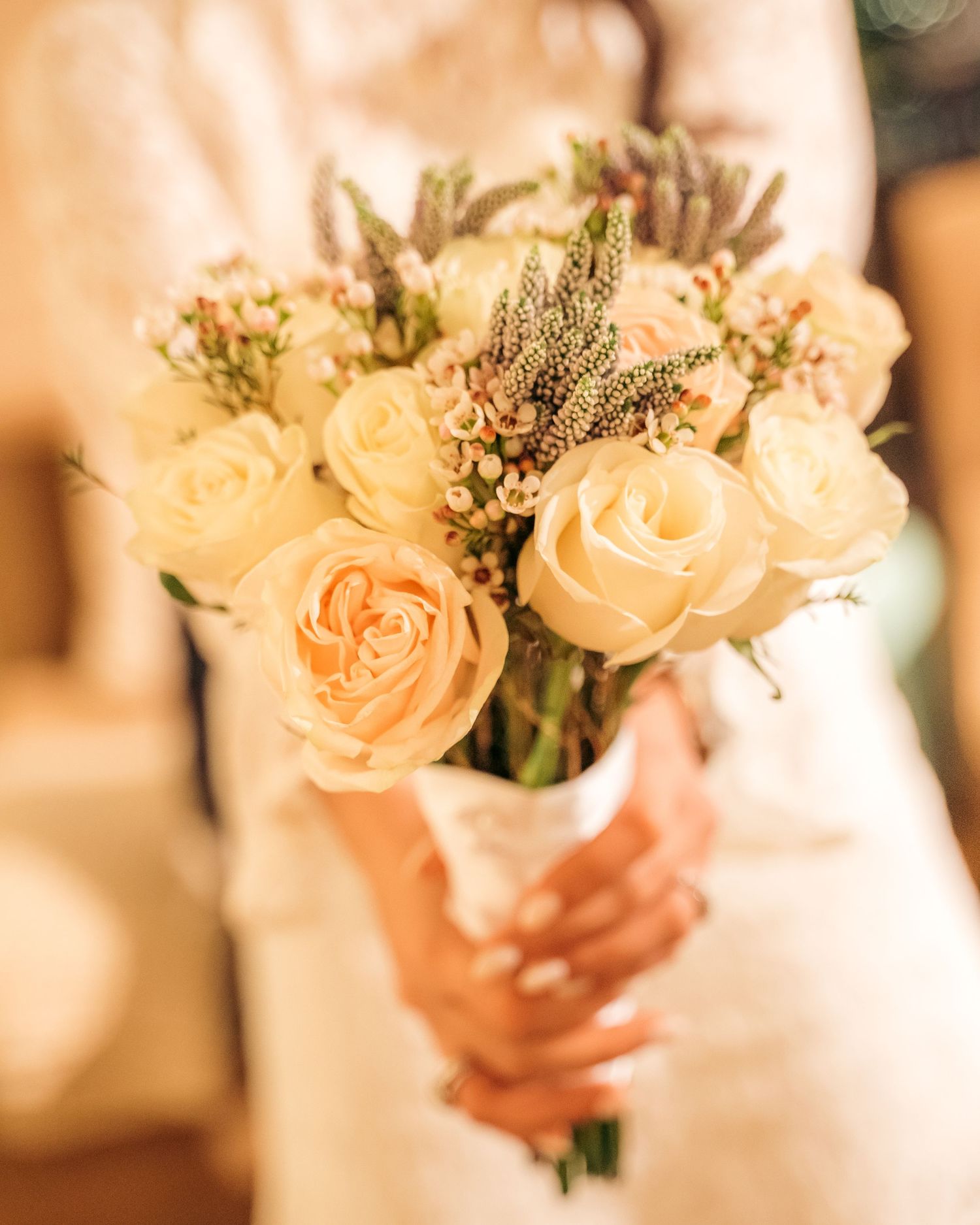 Bride holding elegant white rose and lavender wedding bouquet with delicate floral arrangement.