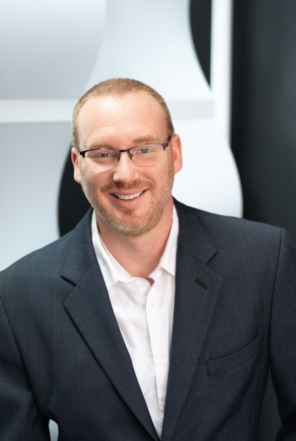 Business professional in dark suit and glasses smiling against white office background. Quad Cities Business Headshot Photography