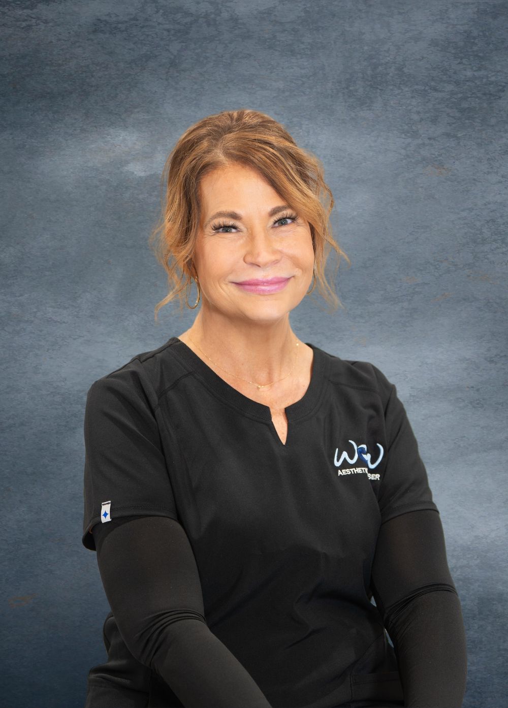 Healthcare worker wearing black uniform with logo against blue background. Quad Cities Business Headshot Photography