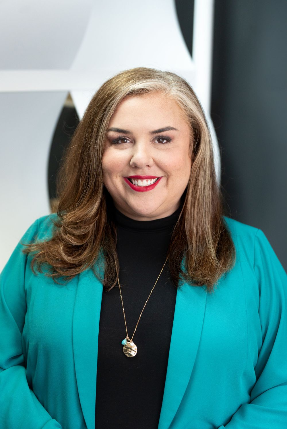 Professional wearing teal blazer and black turtleneck with pendant necklace against white background. Quad Cities Business Headshot Photogra