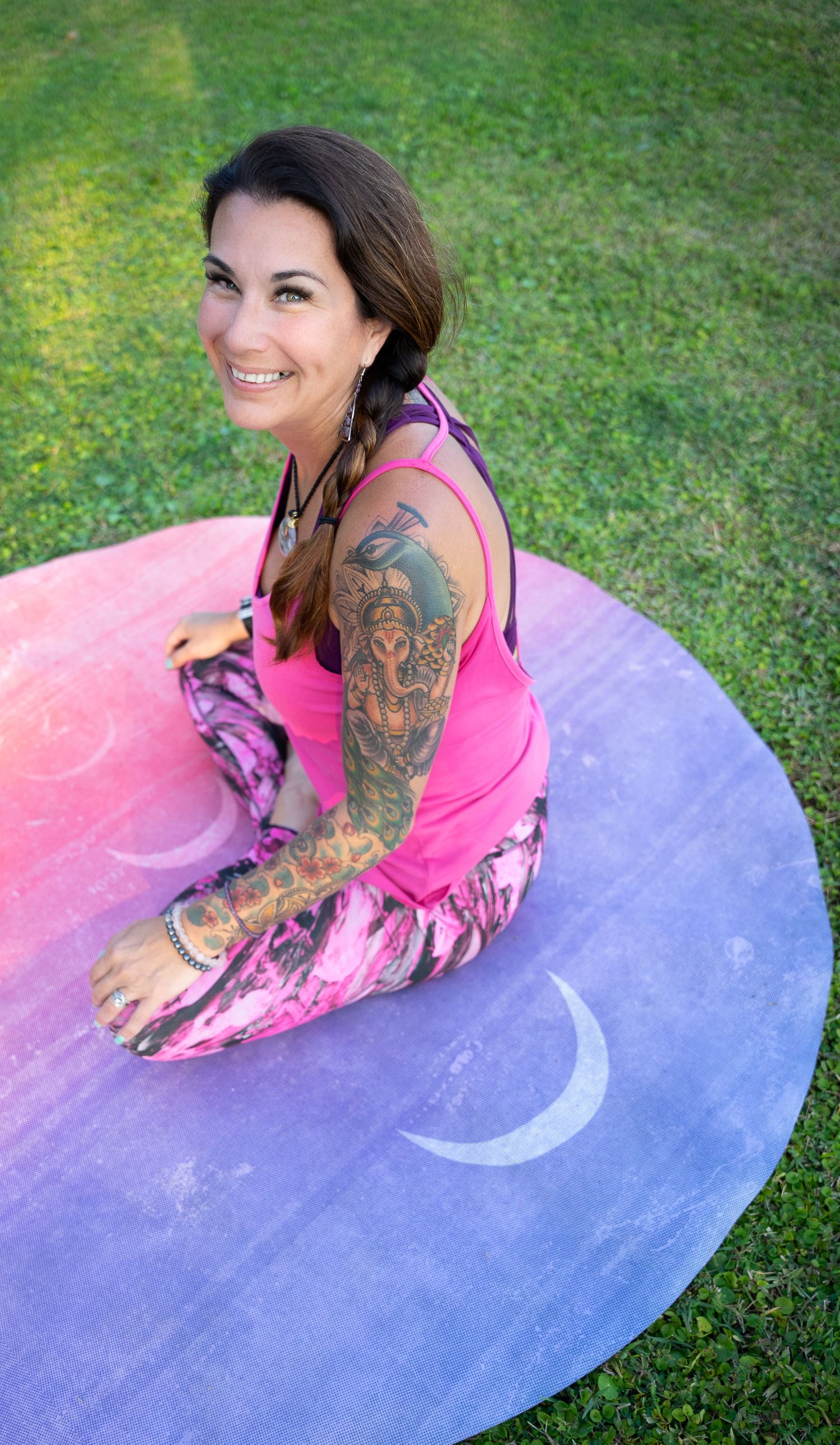 Someone sitting on a purple circular mat outdoors on green grass.