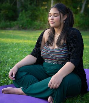 Person in dark dress resting on purple yoga mat in a peaceful outdoor setting.