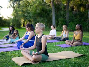 Group of people practicing yoga outdoors on colorful mats in a park setting.