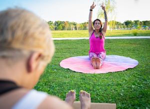 Group yoga class stretching outdoors on colorful mats in a grassy park setting.