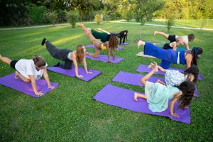 Group yoga class practicing stretching exercises on colorful mats in park.